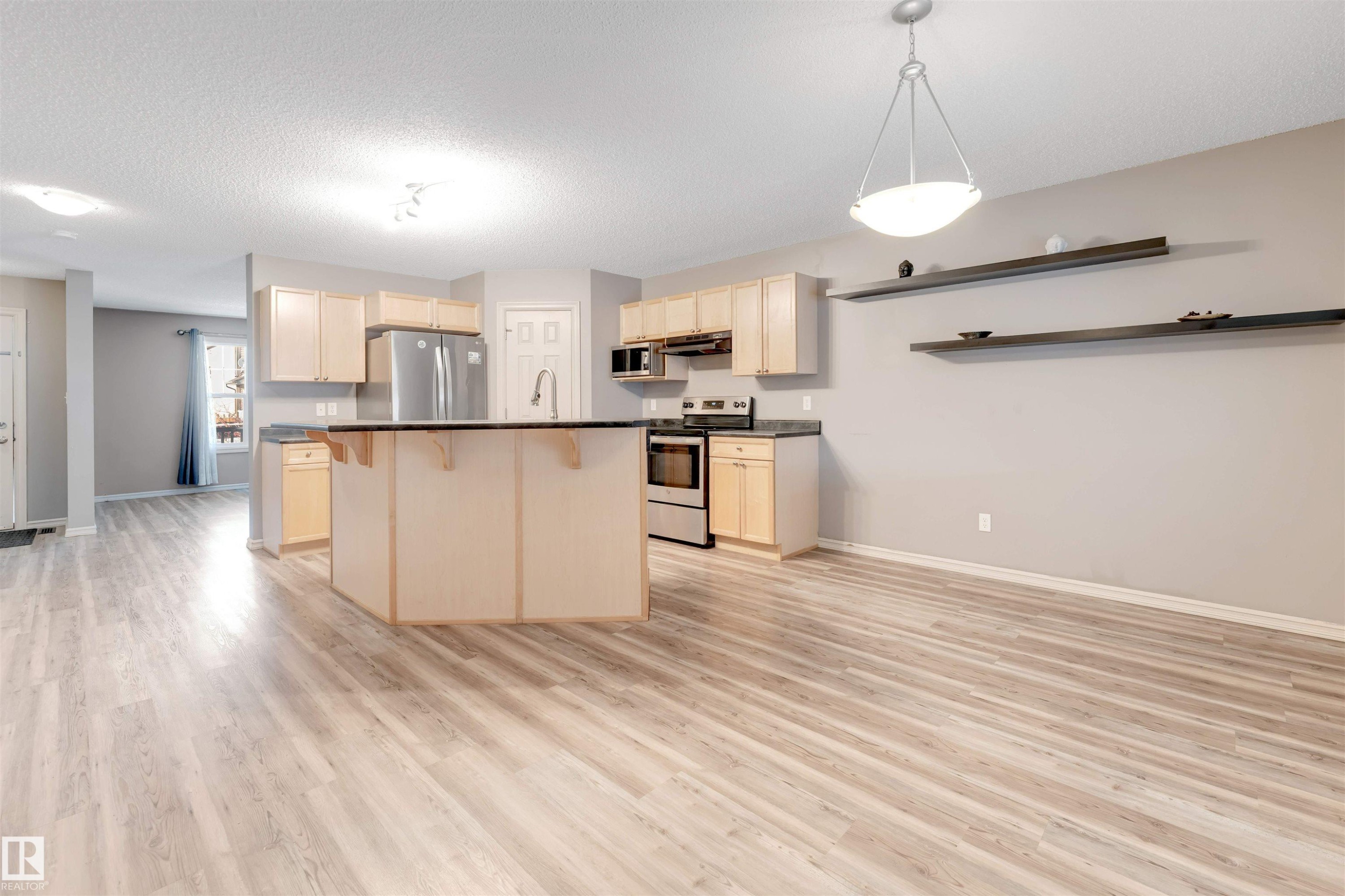 Kitchen with a kitchen bar, a center island, stainless steel appliances, dark countertops, and light wood finished floors - 1157 37 Avenue, Edmonton, AB - Indoor Photo Showing Kitchen