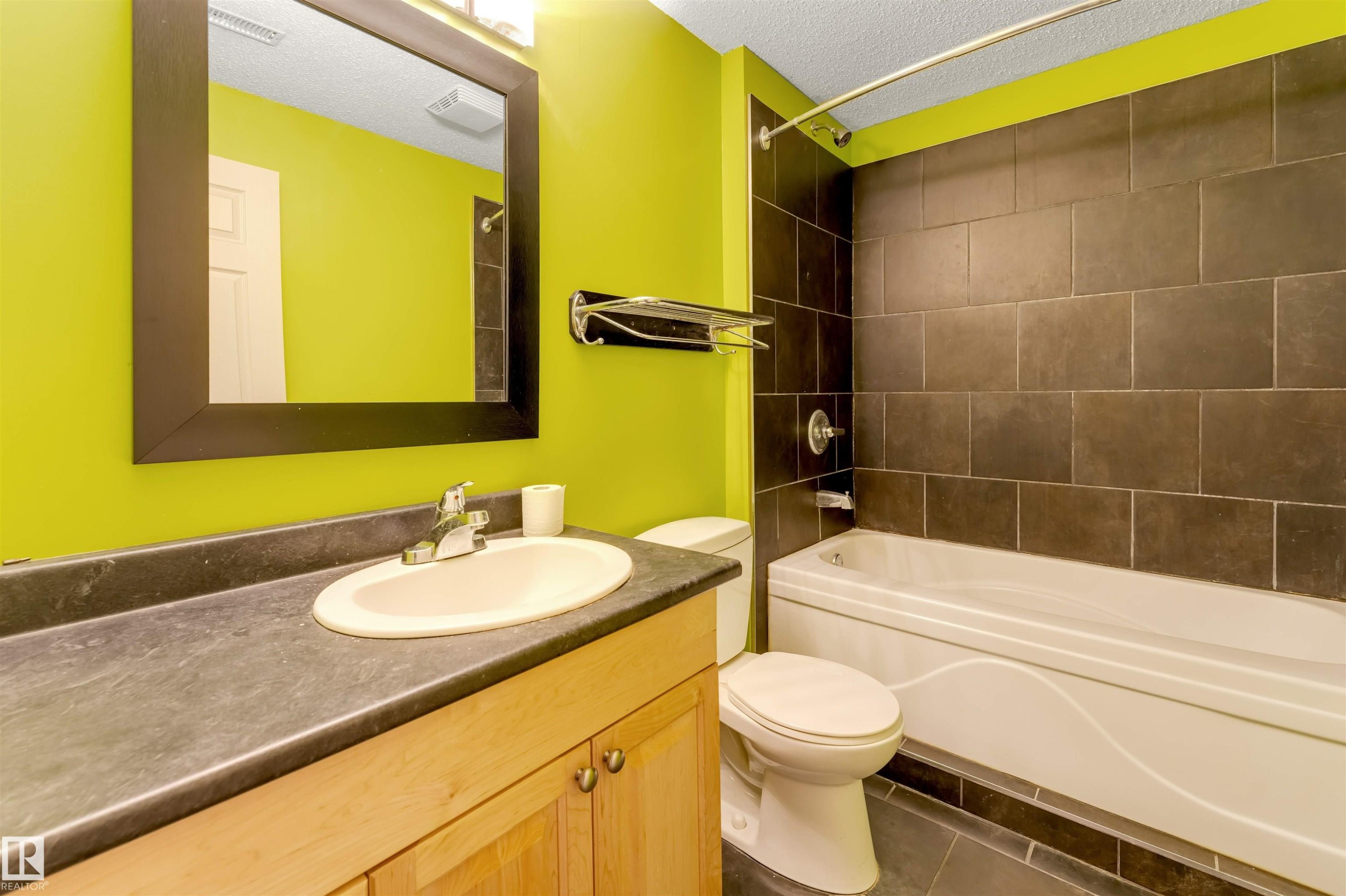 Full bath featuring vanity, a textured ceiling, bathtub / shower combination, and dark tile patterned floors - 1157 37 Avenue, Edmonton, AB - Indoor Photo Showing Bathroom
