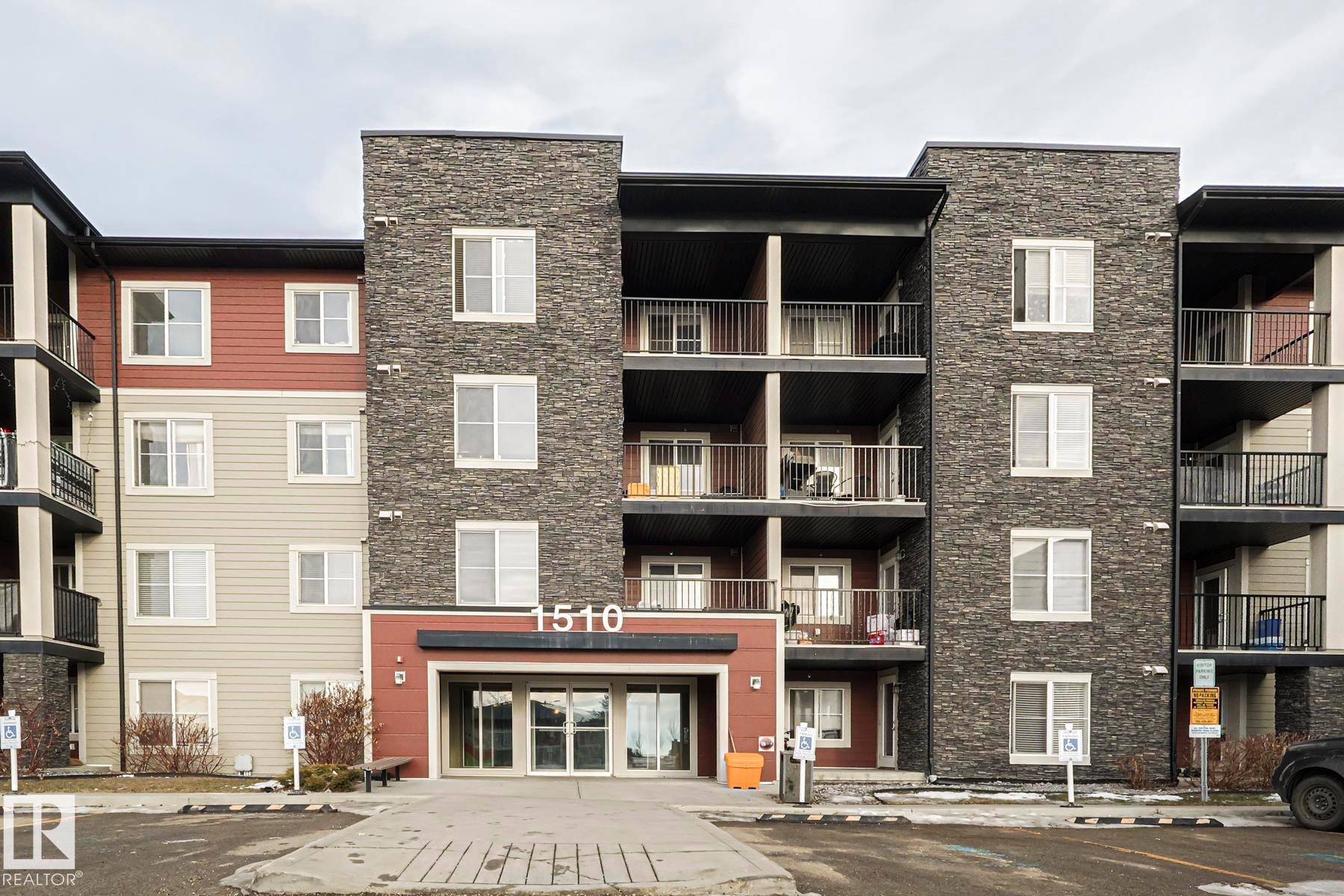 The property features a multi-story exterior with a combination of stone veneer and siding, private balconies with dark railings, and a prominent main entrance with large glass doors - 313 1510 Watt Drive, Edmonton, AB - Outdoor With Balcony With Facade