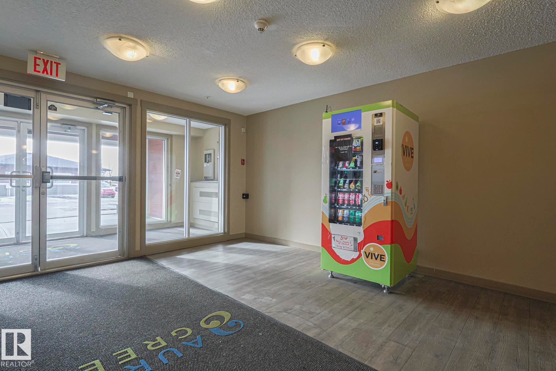 The property features a well-lit entrance with glass doors and a grey floor mat - 313 1510 Watt Drive, Edmonton, AB - Indoor Photo Showing Other Room