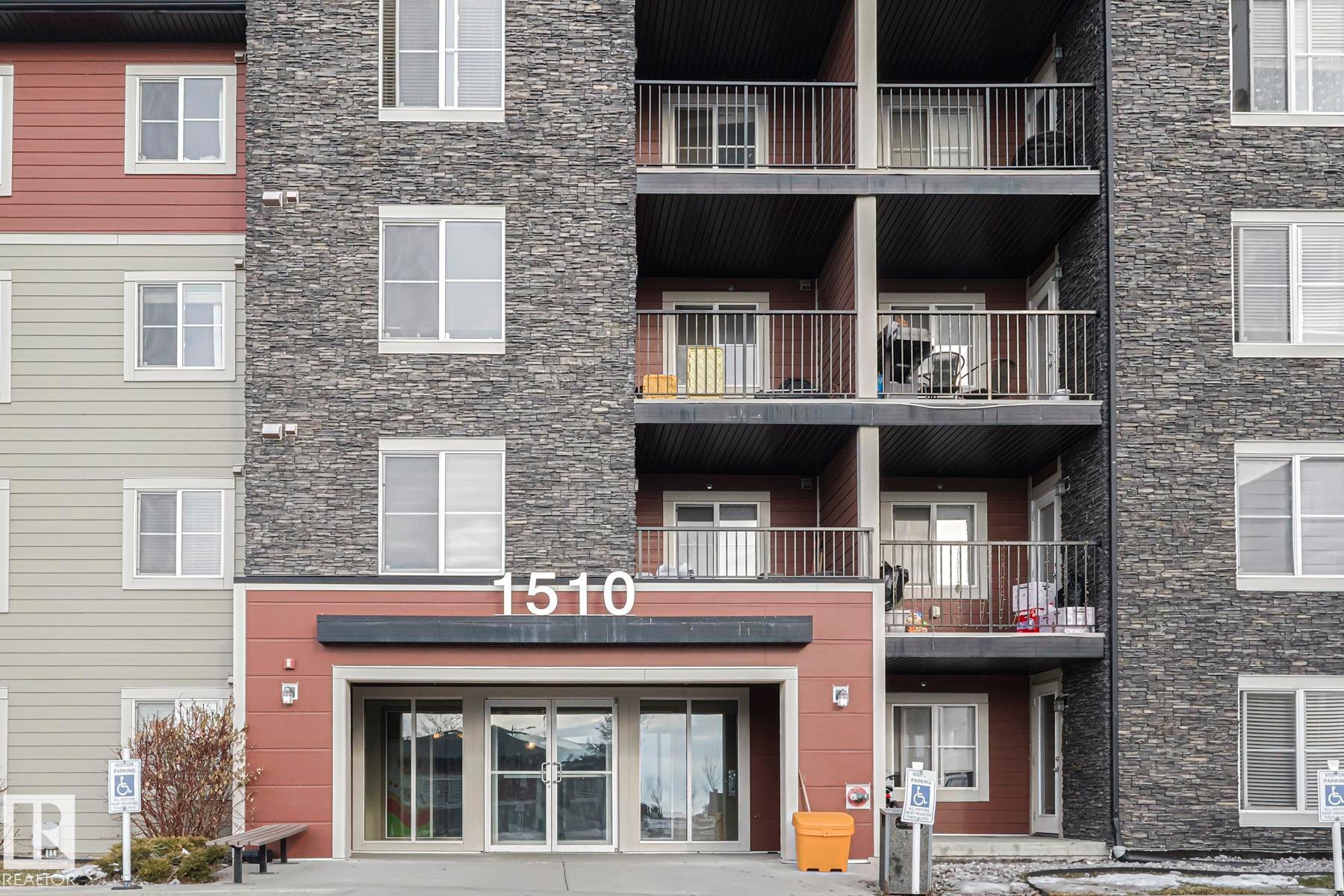 The building features a stone facade and red siding accents - 313 1510 Watt Drive, Edmonton, AB - Outdoor With Balcony With Facade