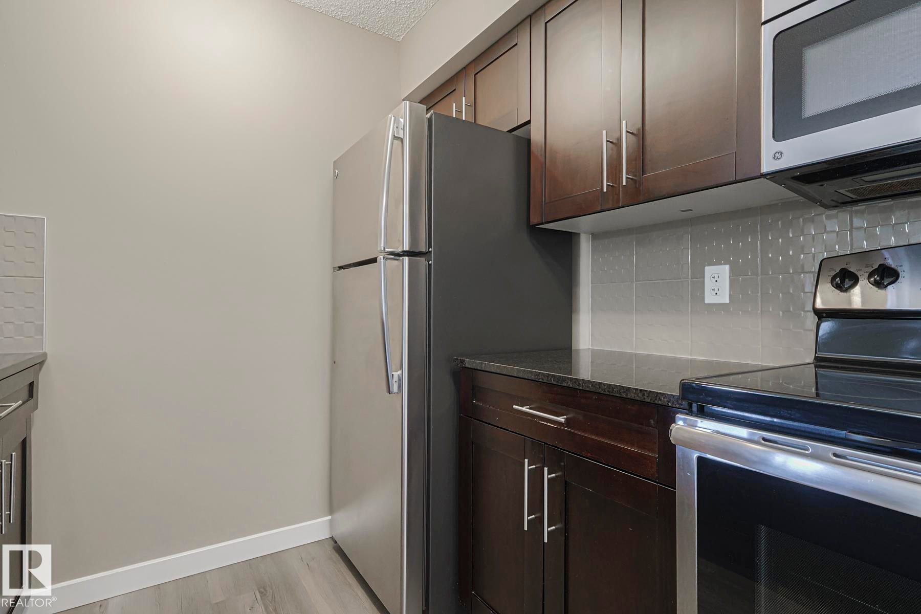 The kitchen features dark wood cabinetry, stainless steel appliances, and a tiled backsplash - 313 1510 Watt Drive, Edmonton, AB - Indoor Photo Showing Kitchen