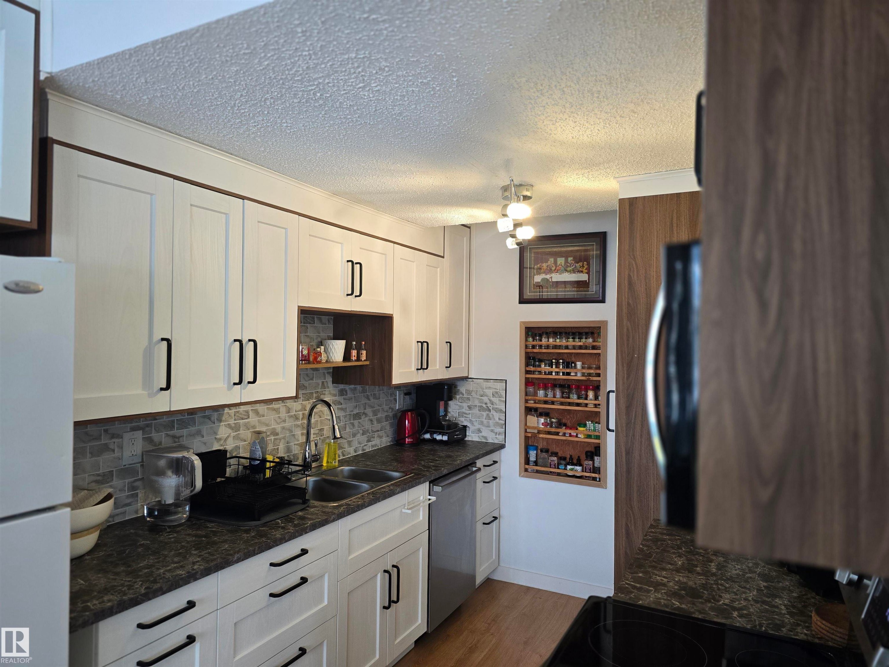 The kitchen features white cabinetry with dark hardware, a double basin sink, and a tiled backsplash - 80 Amberly Crest, Edmonton, AB - Indoor Photo Showing Kitchen With Double Sink