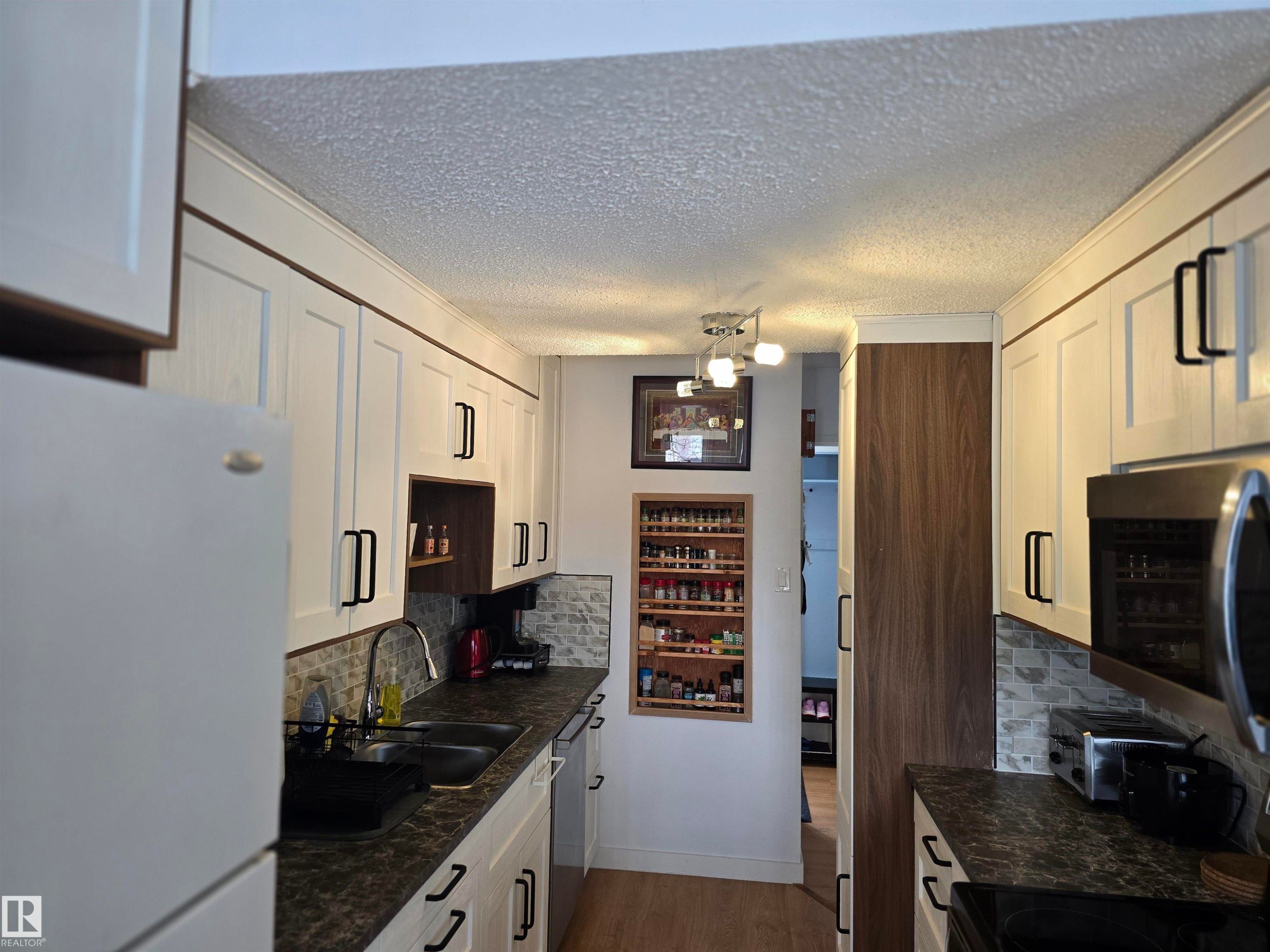 Kitchen featuring white cabinetry with dark hardware, dark countertops, a stainless steel sink, and a tiled backsplash - 80 Amberly Crest, Edmonton, AB - Indoor Photo Showing Kitchen With Double Sink