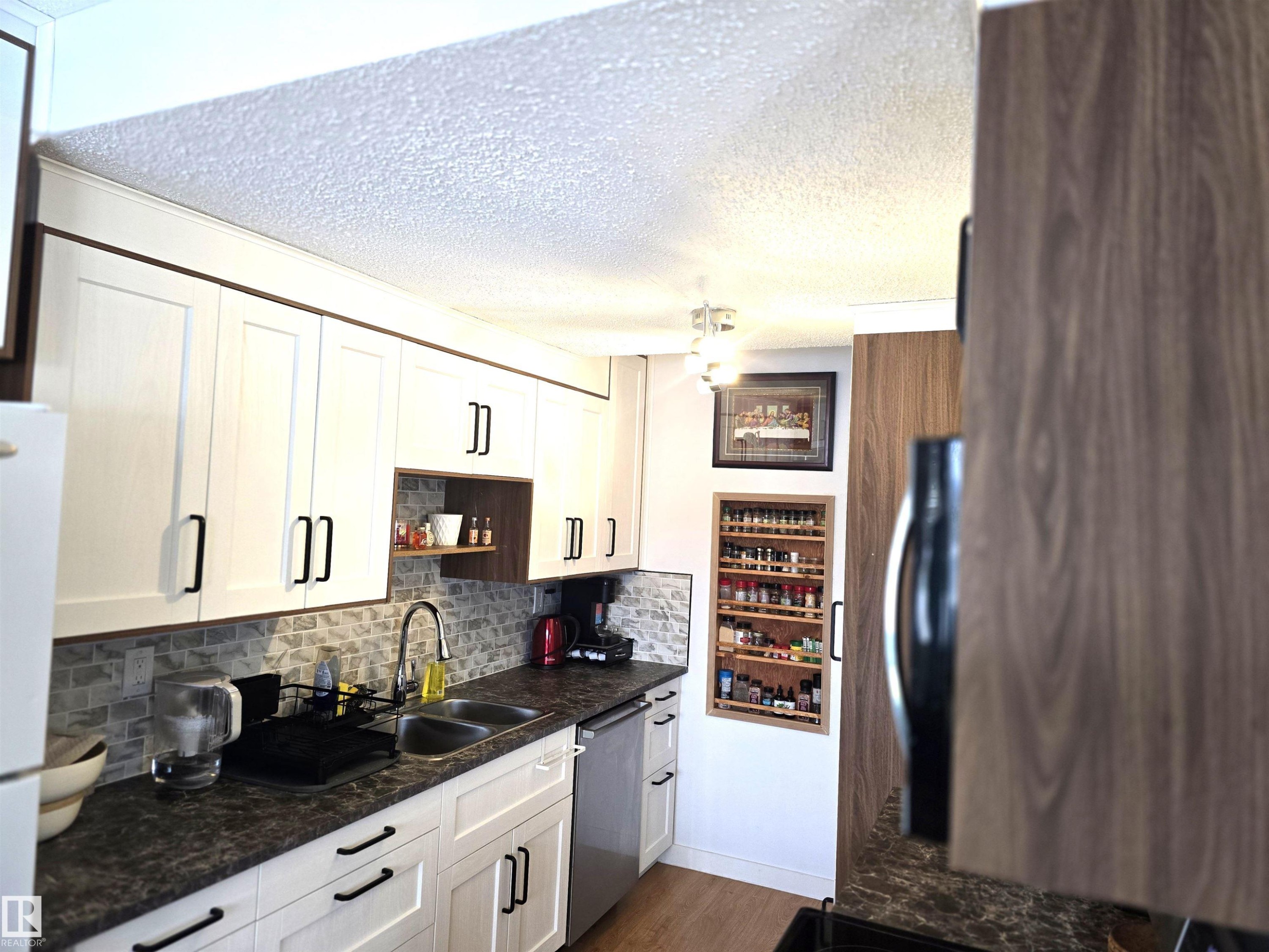 The kitchen features white cabinetry with black hardware, a stainless steel sink, and a tiled backsplash - 80 Amberly Crest, Edmonton, AB - Indoor Photo Showing Kitchen With Double Sink