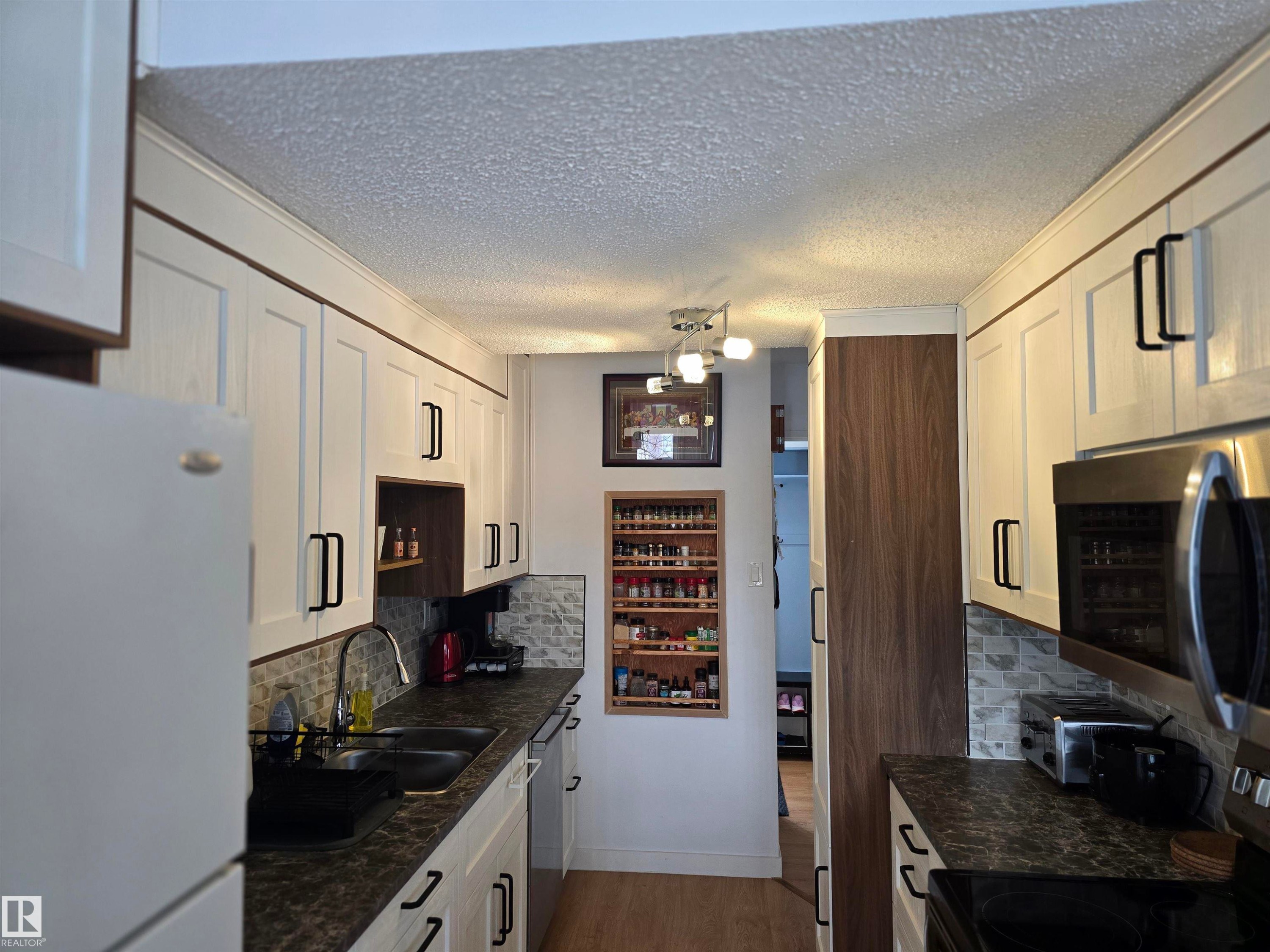 Galley kitchen featuring white cabinetry with black hardware, a stainless steel microwave, and dark countertops - 80 Amberly Crest, Edmonton, AB - Indoor Photo Showing Kitchen With Double Sink