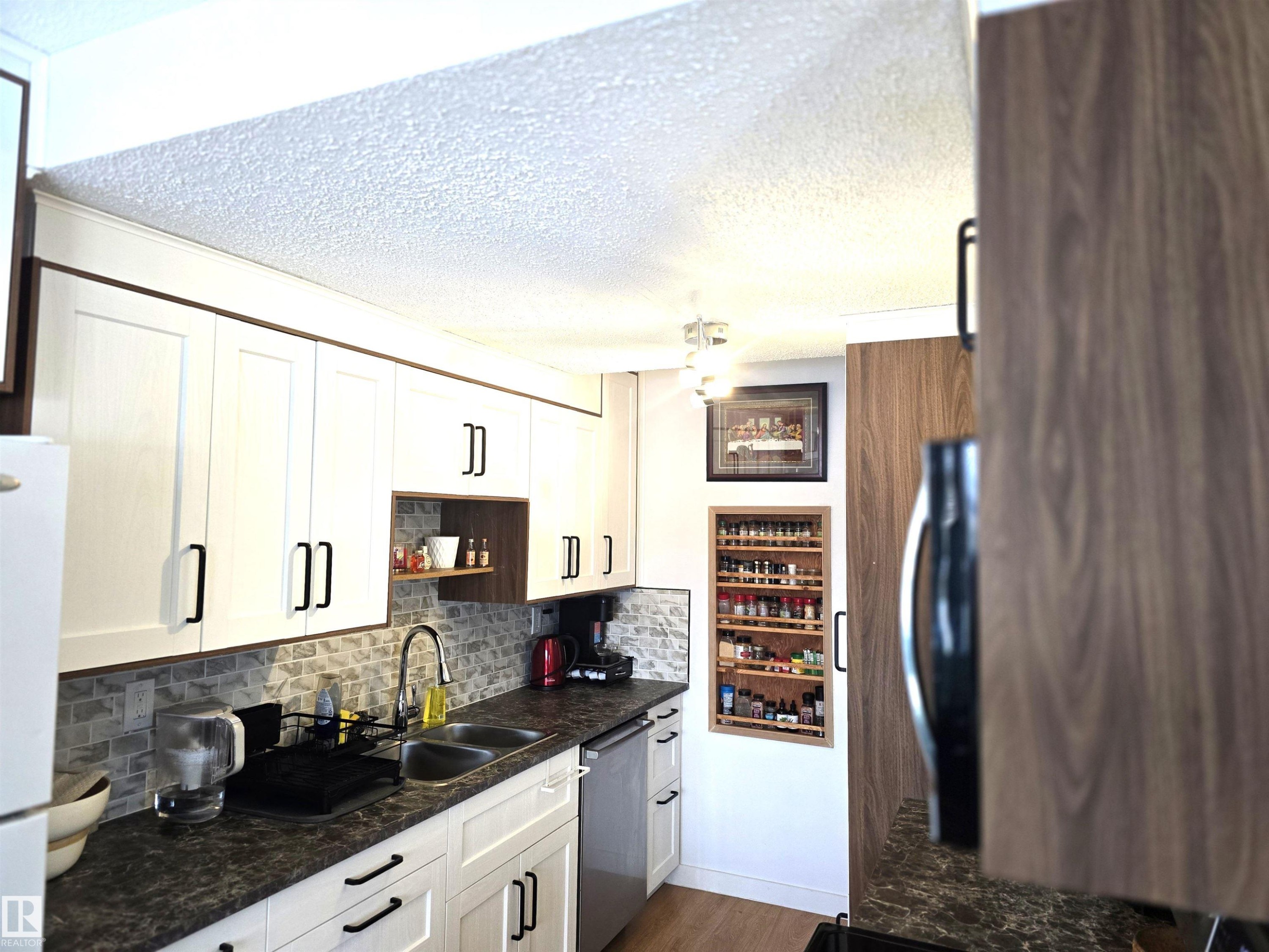 The kitchen features white cabinetry with dark hardware, a stainless steel sink, and a tiled backsplash - 80 Amberly Crest, Edmonton, AB - Indoor Photo Showing Kitchen With Double Sink