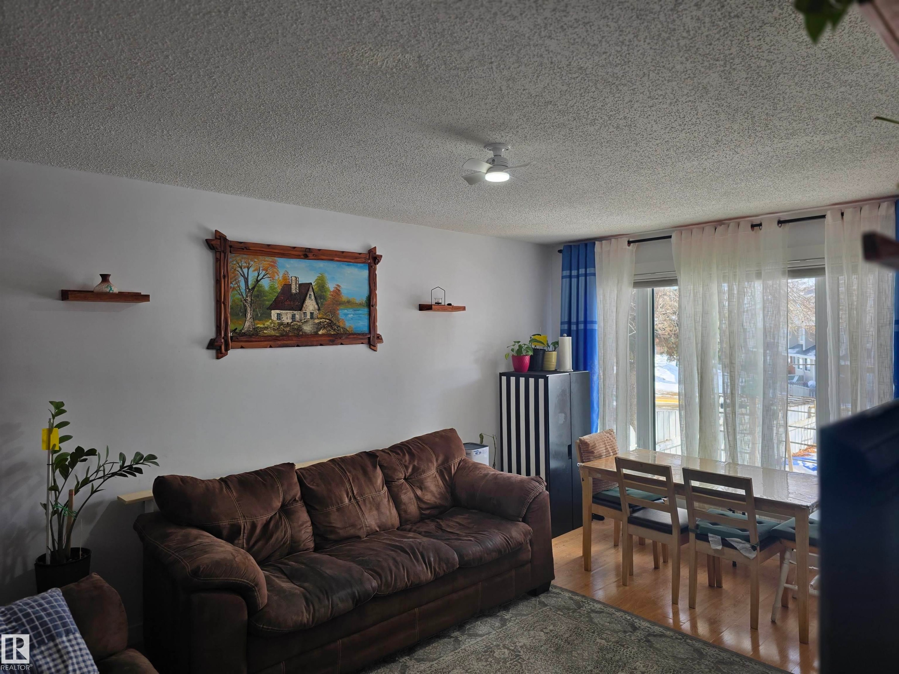 The open-concept living and dining area features white walls, a ceiling fan, and large windows with privacy curtains - 80 Amberly Crest, Edmonton, AB - Indoor Photo Showing Living Room
