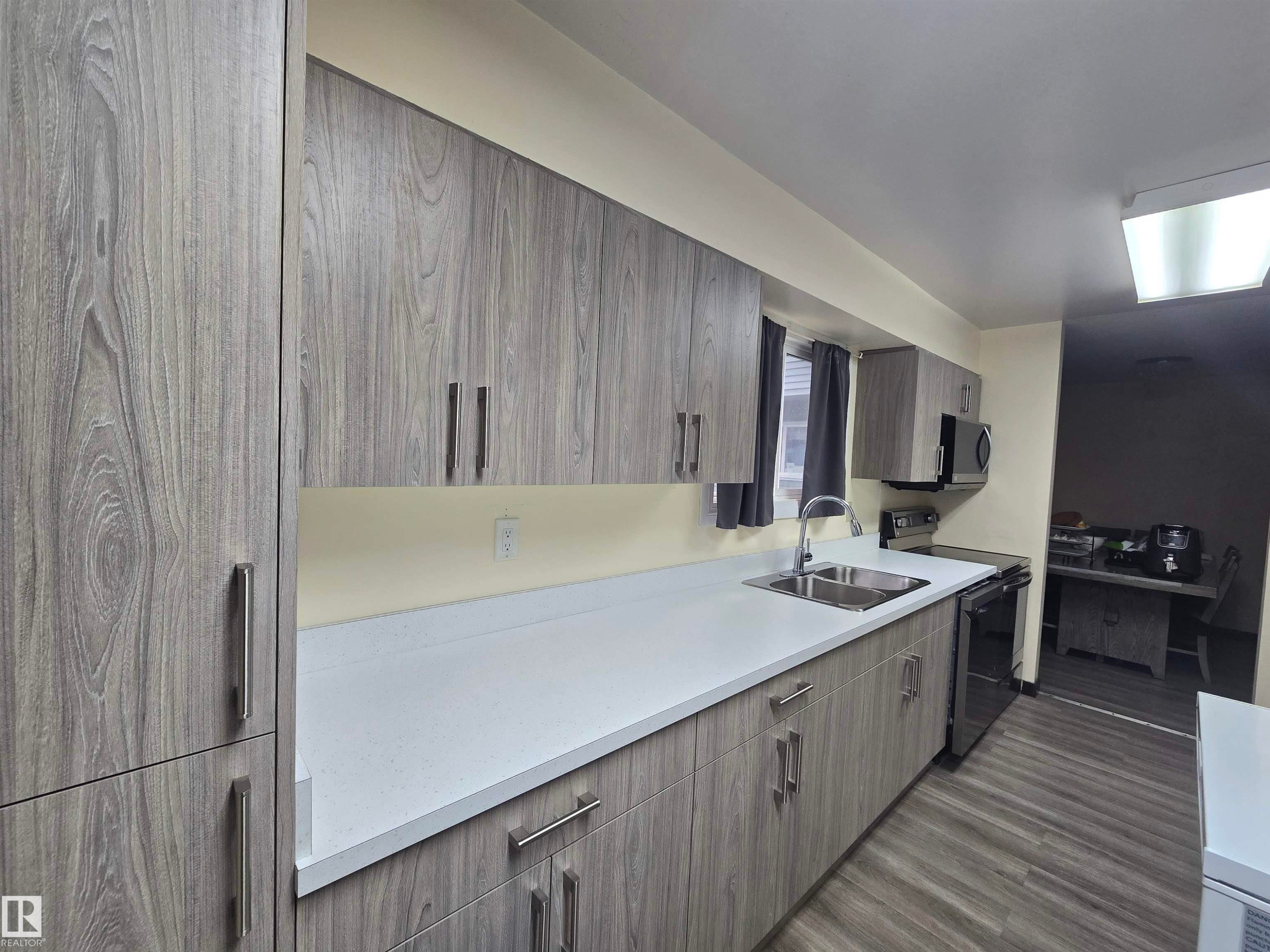 Contemporary kitchen featuring extensive wood-finish cabinetry, light-toned countertops, a stainless steel double basin sink, and wood-finish flooring - 2 4403 Riverbend Road, Edmonton, AB