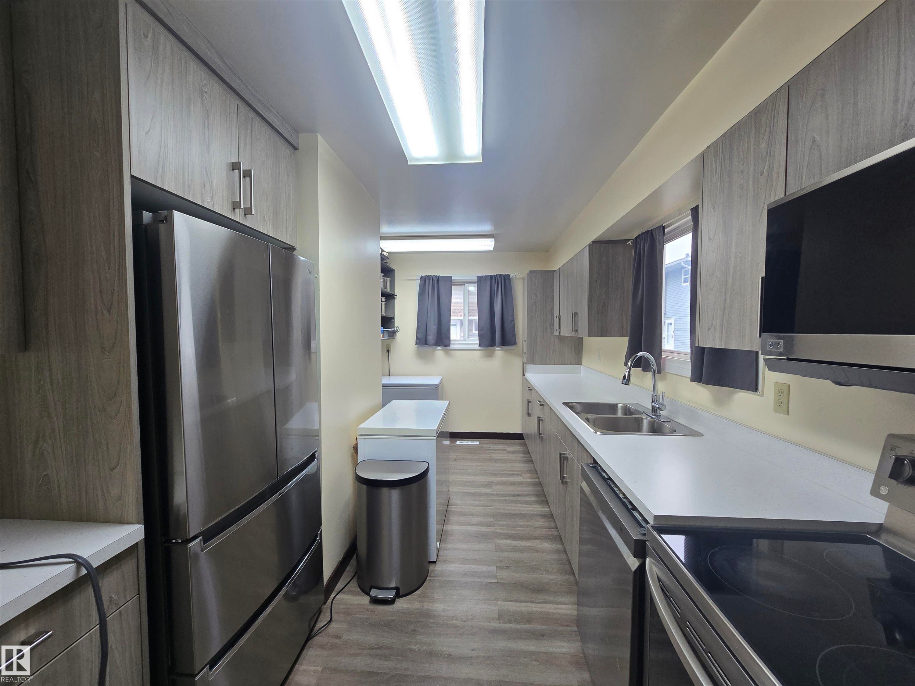 Galley kitchen featuring wood-grain cabinetry, stainless steel appliances, and wood-finish flooring - 2 4403 Riverbend Road, Edmonton, AB