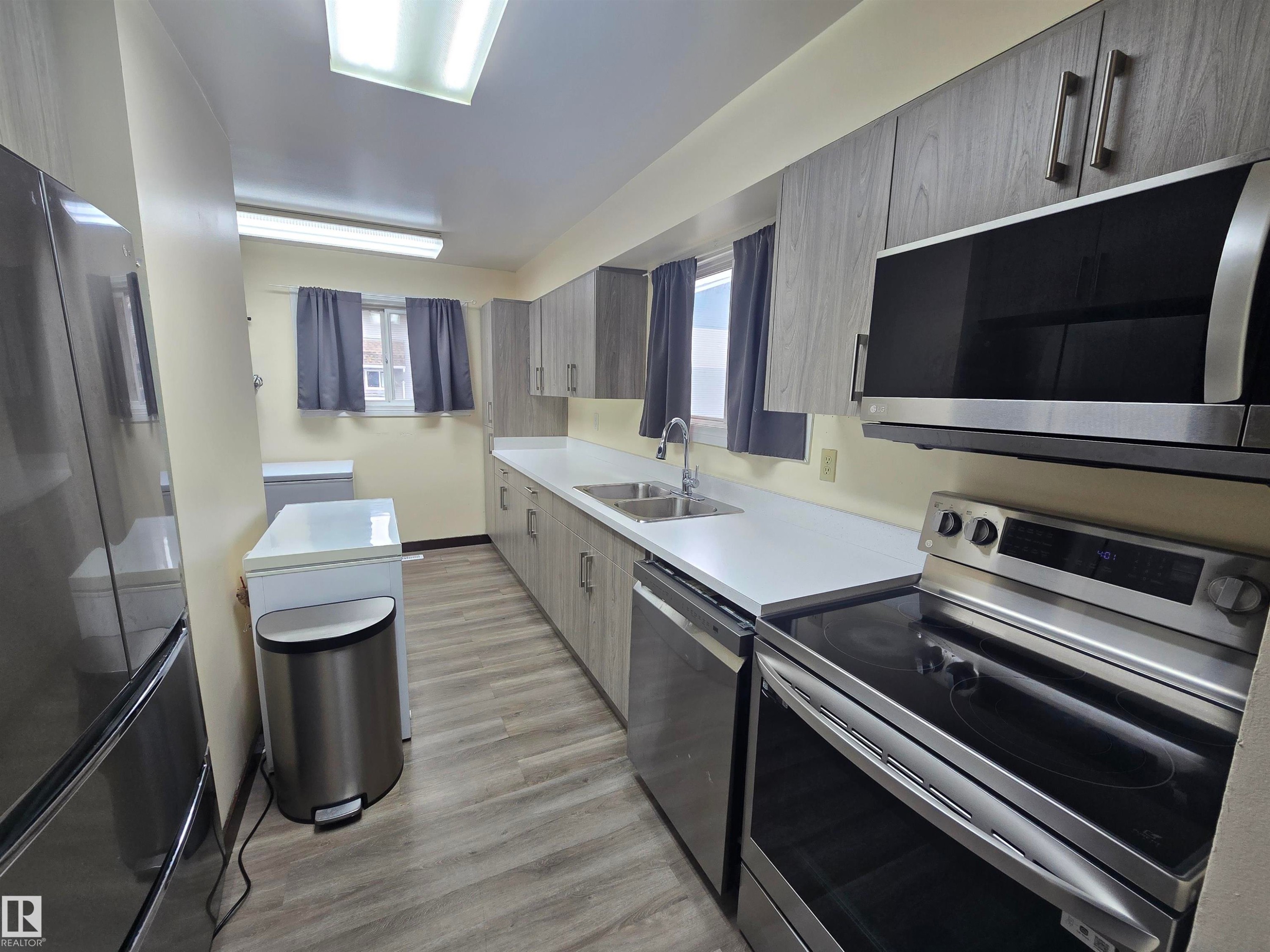 Contemporary kitchen featuring wood-finish cabinetry, stainless steel appliances, a double basin sink, and wood-finish flooring - 2 4403 Riverbend Road, Edmonton, AB