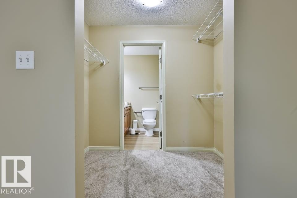 Carpeted walk-in closet featuring wire shelving and direct access to a bathroom with wood-finish flooring - #107 4903 47 Av, Stony Plain, AB - Indoor