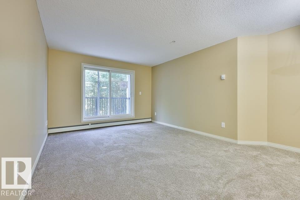 Spacious room featuring light-toned walls and carpet flooring - #107 4903 47 Av, Stony Plain, AB - Indoor Photo Showing Other Room