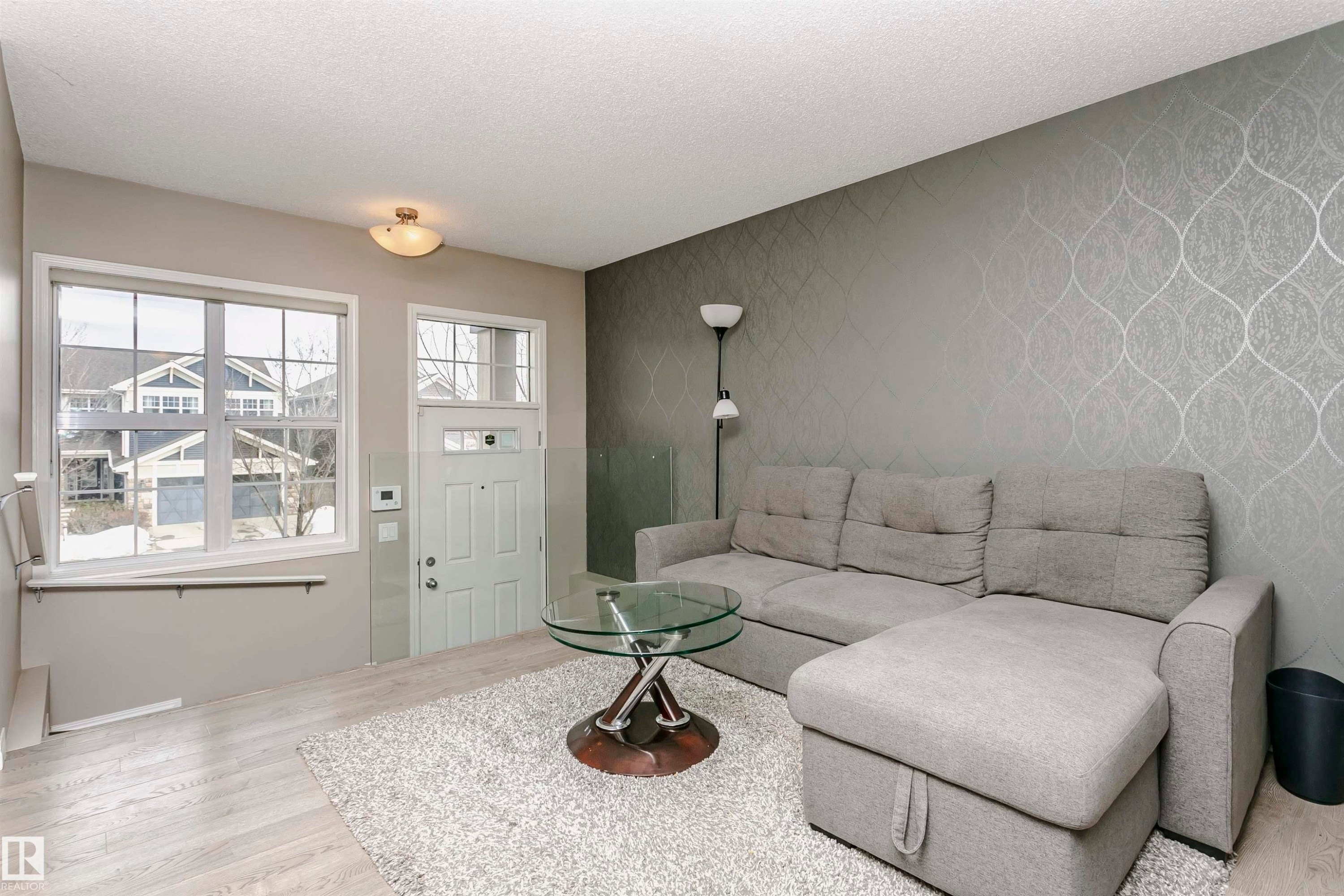 Living area featuring light wood-style floors, an accent wall, a textured ceiling, and wallpapered walls - 4011 Orchards Drive, Edmonton, AB - Indoor