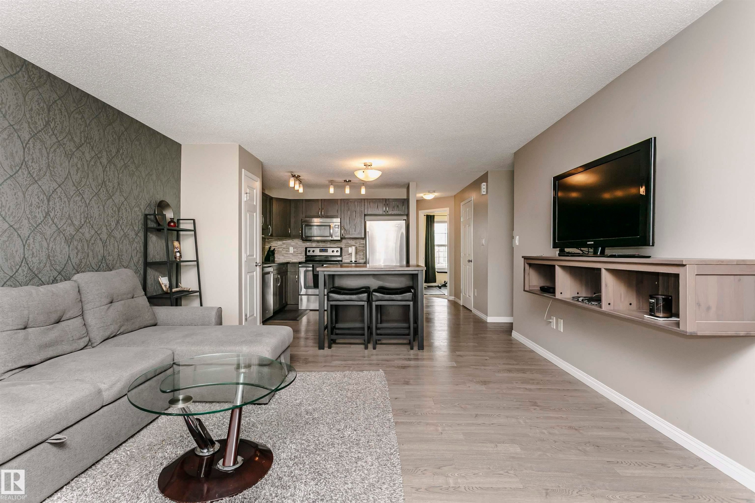 Living area with light wood-style floors, wallpapered walls, an accent wall, and a textured ceiling - 4011 Orchards Drive, Edmonton, AB - Indoor Photo Showing Living Room