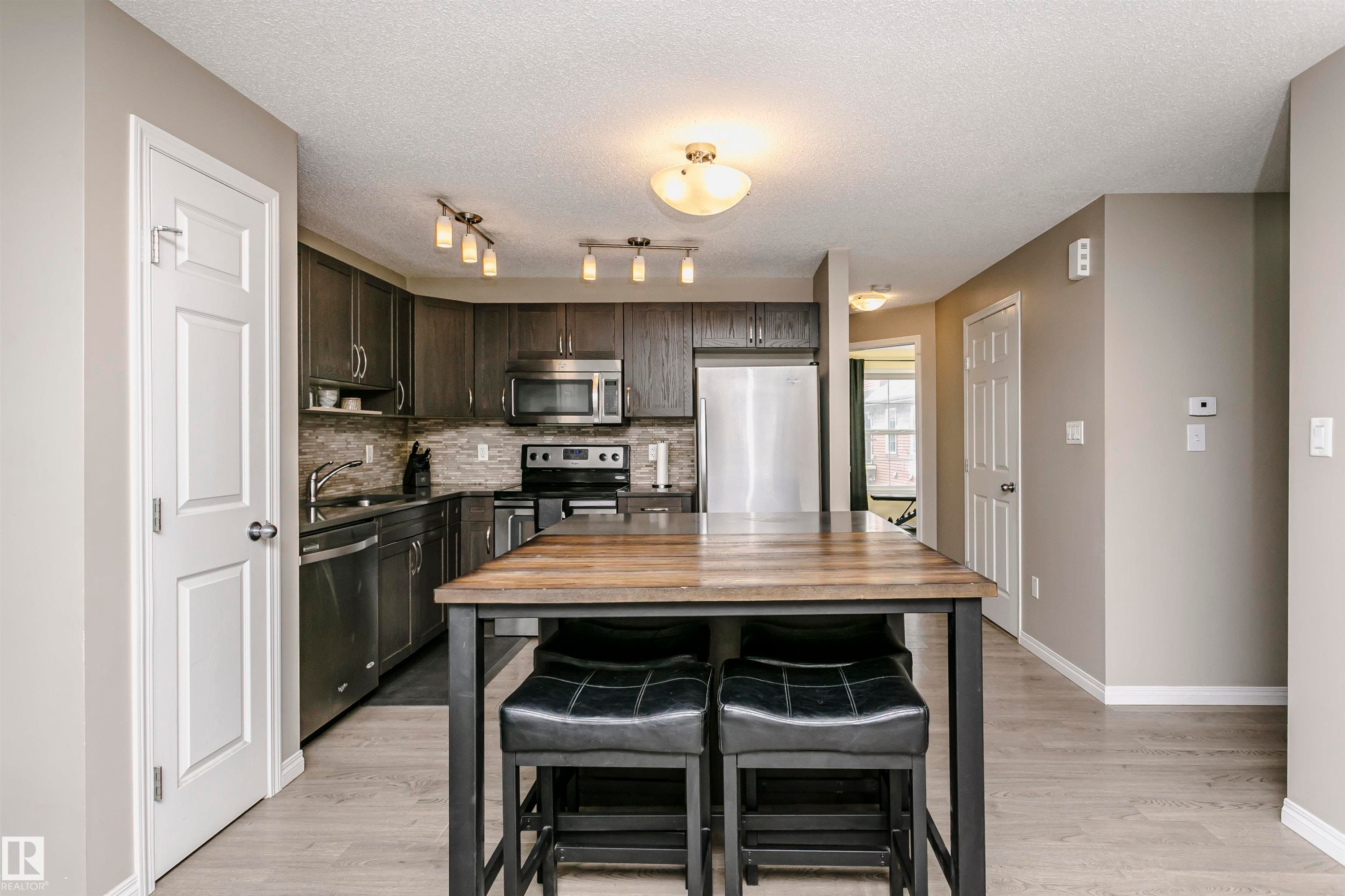 Kitchen with stainless steel appliances, a kitchen bar, backsplash, light wood finished floors, and a textured ceiling - 4011 Orchards Drive, Edmonton, AB - Indoor Photo Showing Kitchen With Stainless Steel Kitchen