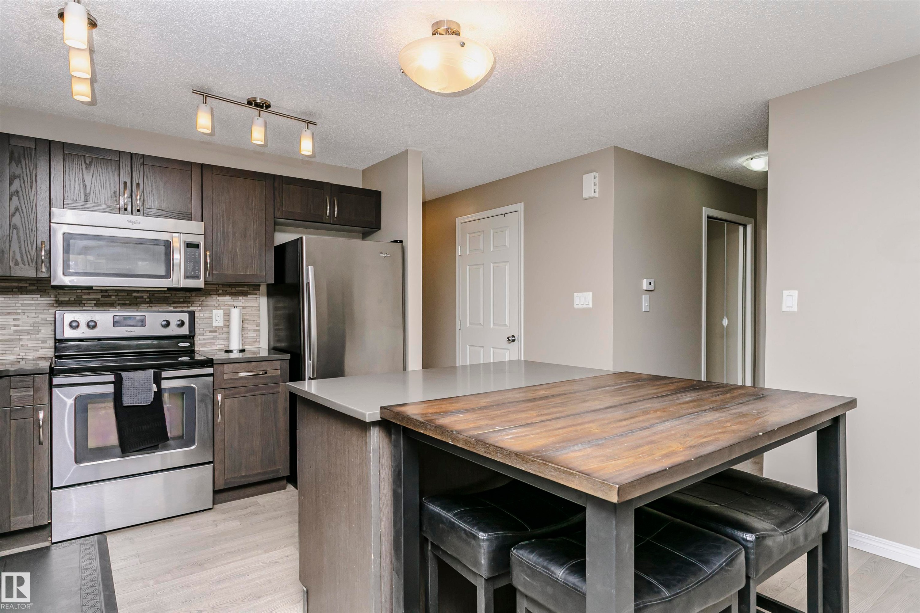 Kitchen featuring wood counters, stainless steel appliances, a breakfast bar, light wood-style flooring, and decorative backsplash - 4011 Orchards Drive, Edmonton, AB - Indoor Photo Showing Kitchen With Stainless Steel Kitchen