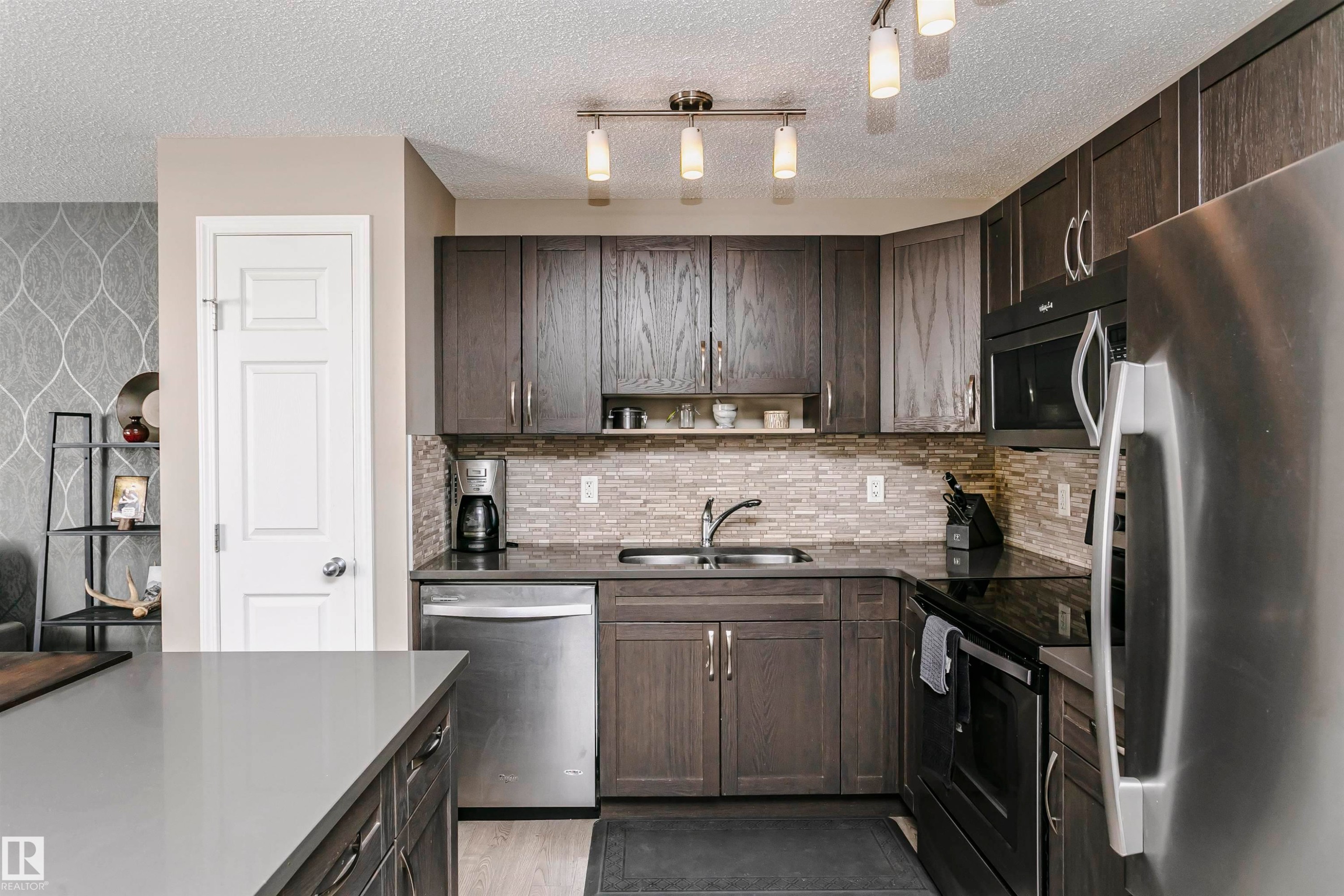 Kitchen featuring stainless steel appliances, open shelves, dark wood finish cabinets, a textured ceiling, and track lighting - 4011 Orchards Drive, Edmonton, AB - Indoor Photo Showing Kitchen With Stainless Steel Kitchen With Double Sink With Upgraded Kitchen