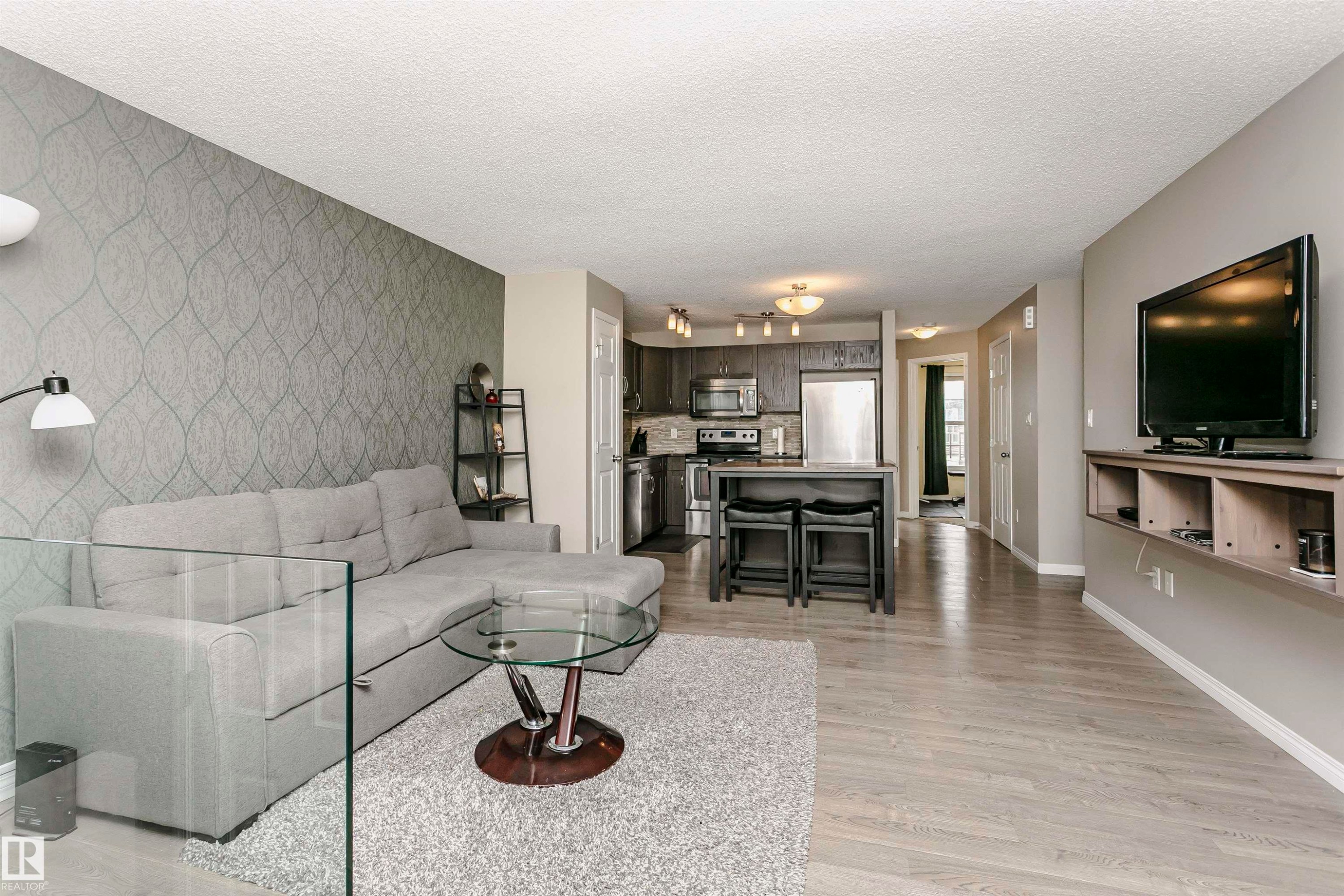 Living room with an accent wall, light wood finished floors, wallpapered walls, and a textured ceiling - 4011 Orchards Drive, Edmonton, AB - Indoor Photo Showing Living Room