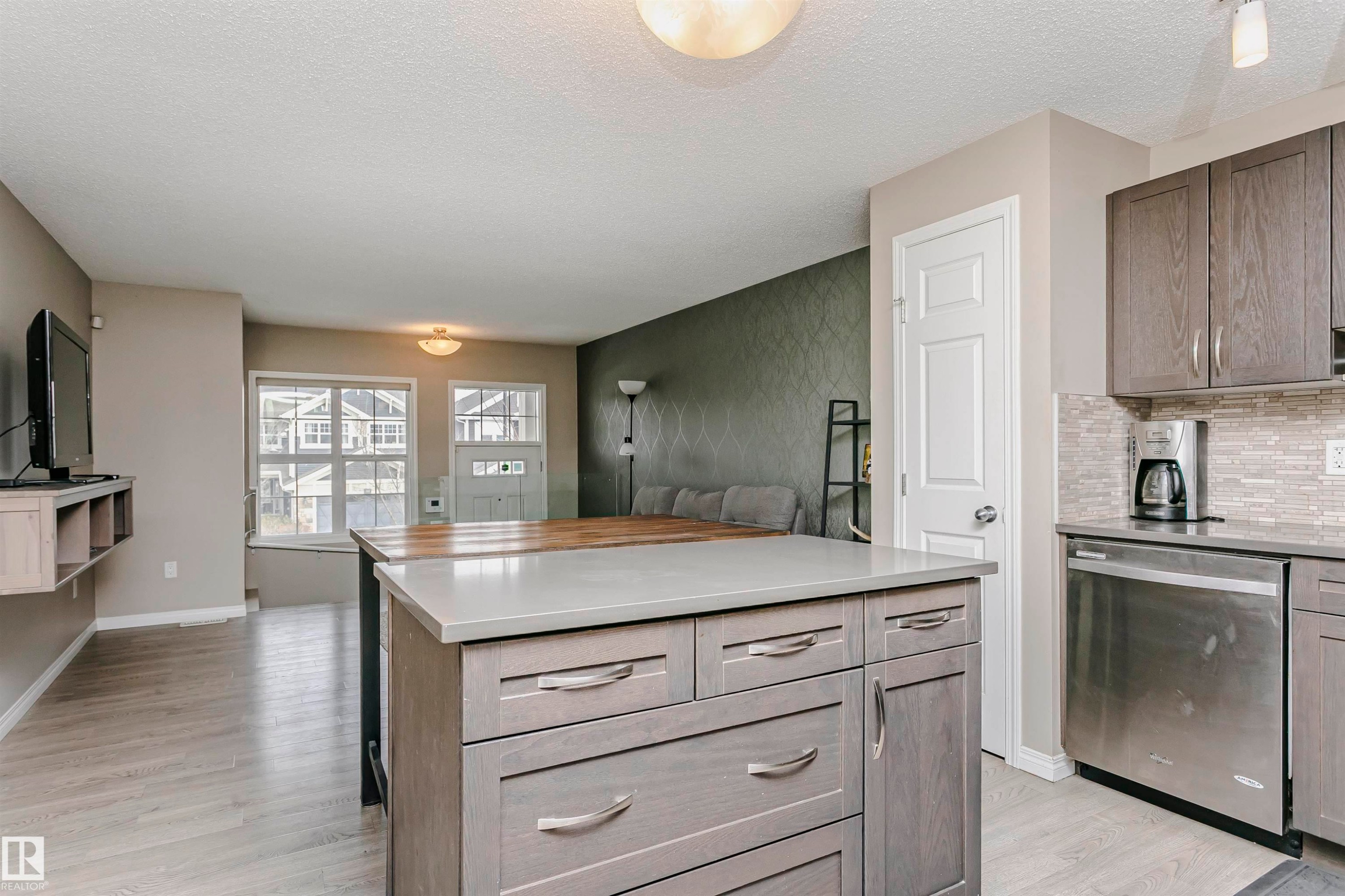 Kitchen with dishwasher, light wood-style flooring, a center island, backsplash, and a textured ceiling - 4011 Orchards Drive, Edmonton, AB - Indoor Photo Showing Kitchen