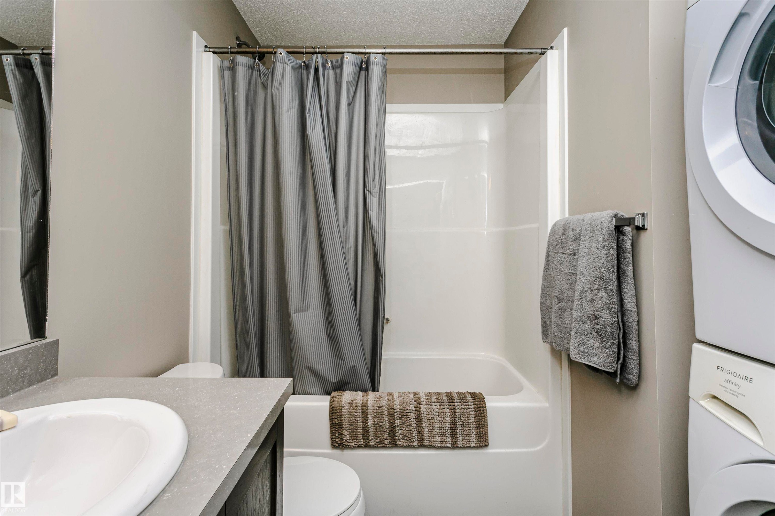 Bathroom featuring vanity, a textured ceiling, stacked washer / drying machine, and shower / bathtub combination with curtain - 4011 Orchards Drive, Edmonton, AB - Indoor