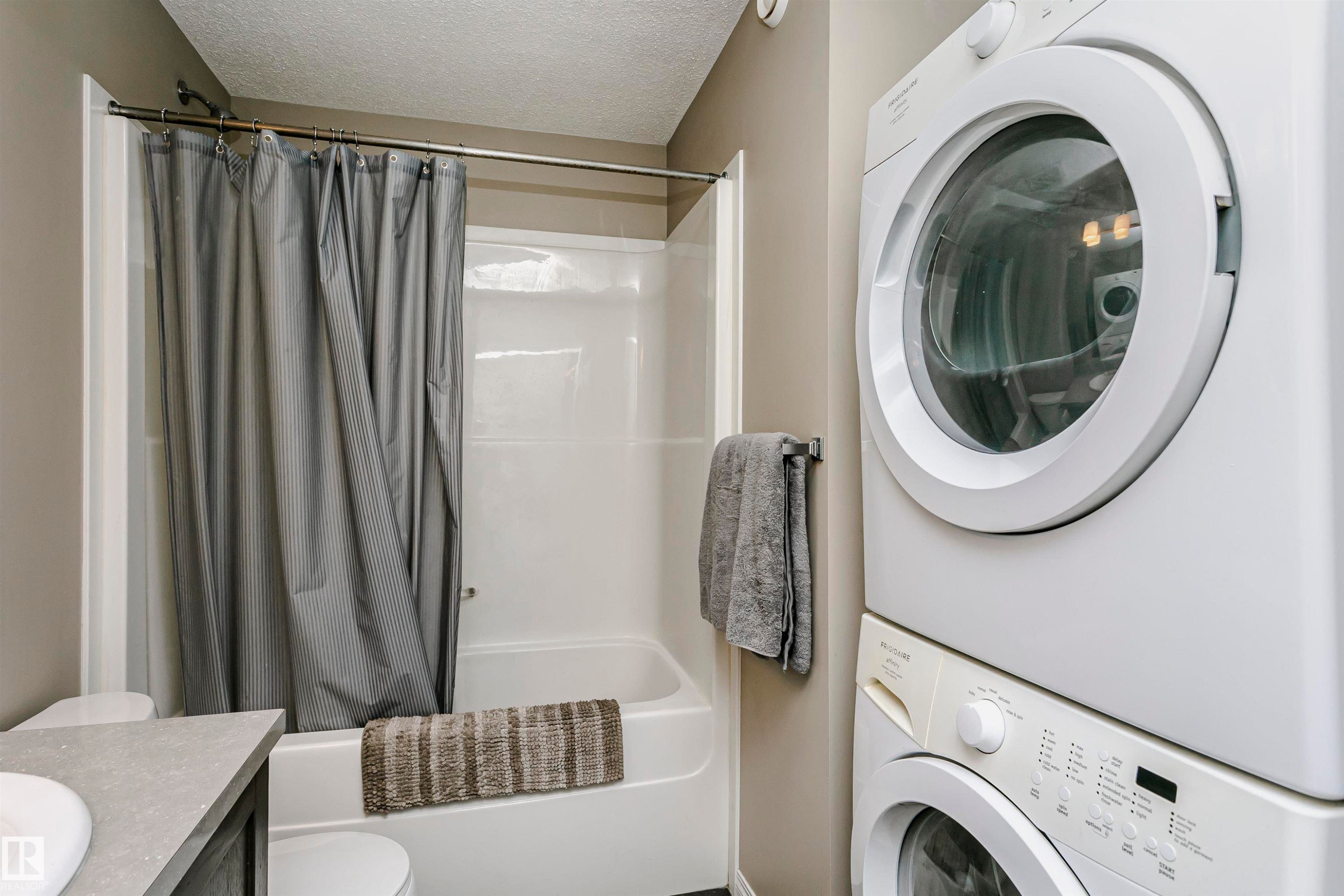 Laundry area with a textured ceiling and stacked washer and dryer - 4011 Orchards Drive, Edmonton, AB - Indoor Photo Showing Laundry Room