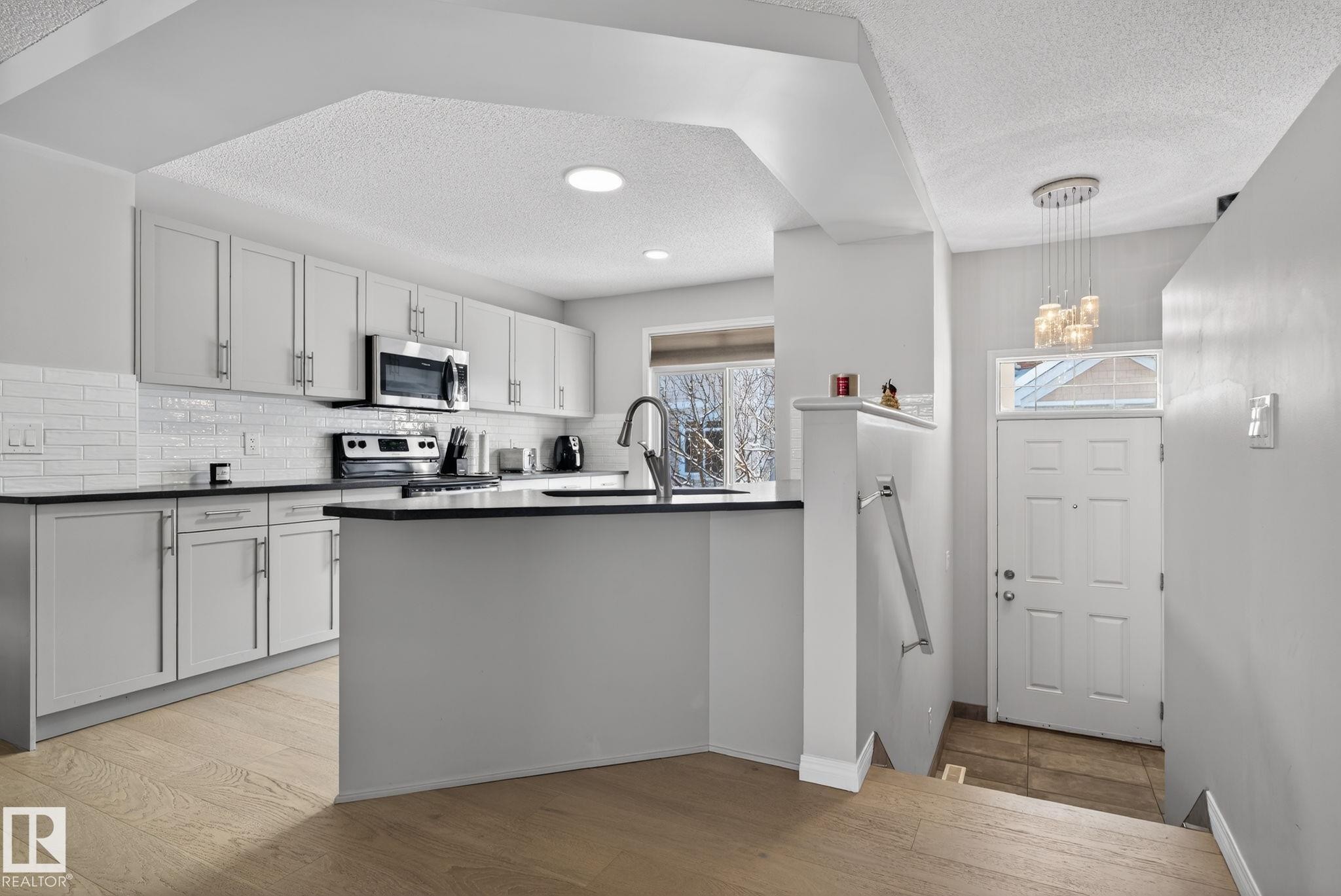 Kitchen with a textured ceiling, stainless steel appliances, light wood-style flooring, a peninsula, and decorative backsplash - 60 1804 70 Street, Edmonton, AB - Indoor Photo Showing Kitchen