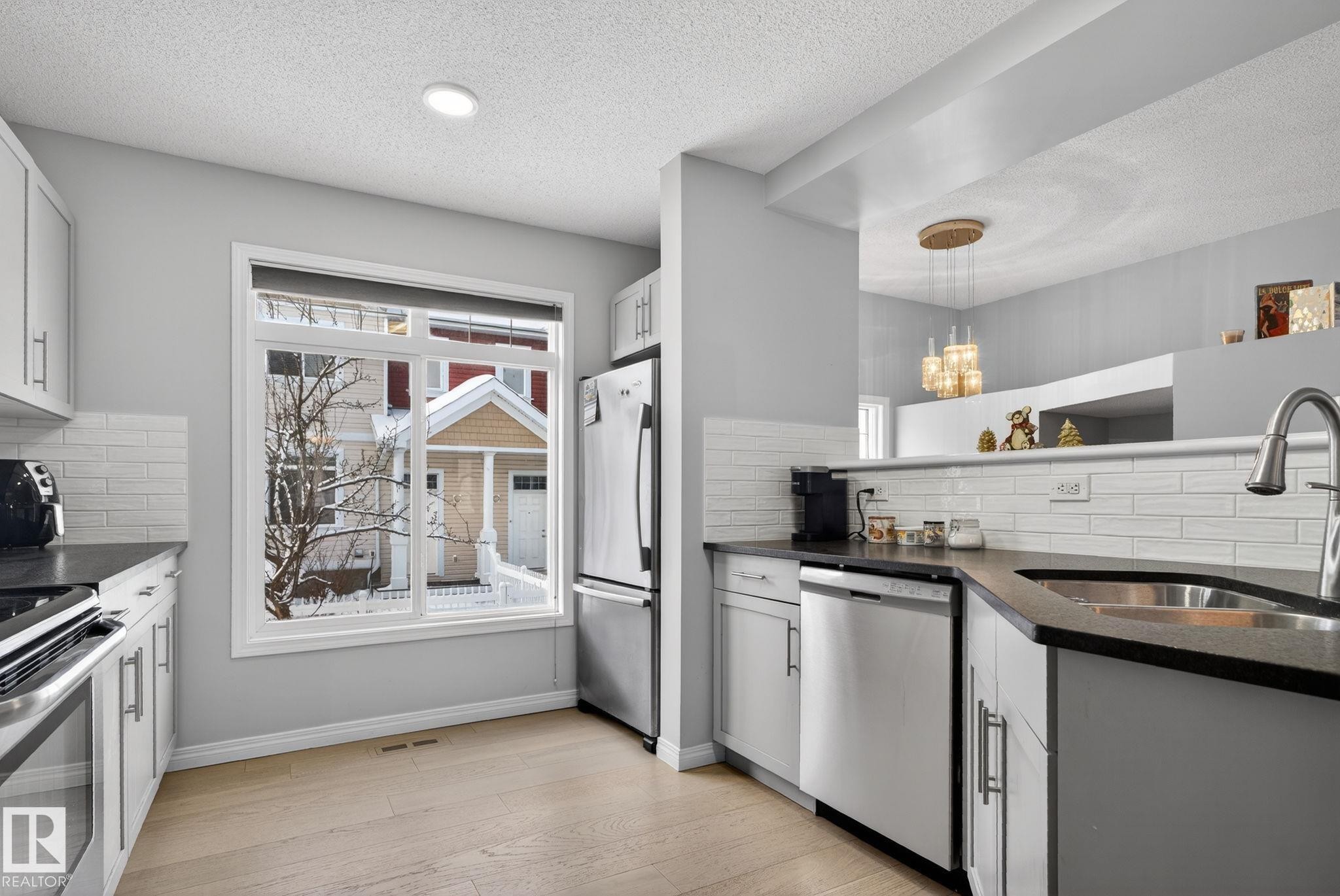 Kitchen with tasteful backsplash, dark stone counters, stainless steel appliances, light wood finished floors, and a textured ceiling - 60 1804 70 Street, Edmonton, AB - Indoor Photo Showing Kitchen