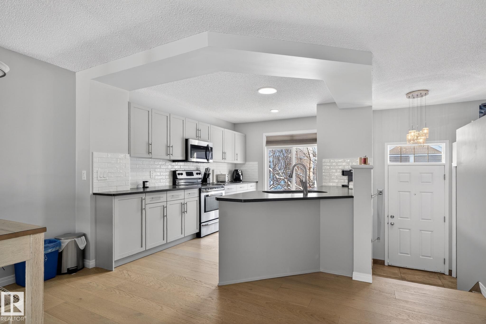 Kitchen with a textured ceiling, stainless steel appliances, a peninsula, light wood-type flooring, and backsplash - 60 1804 70 Street, Edmonton, AB - Indoor Photo Showing Kitchen With Upgraded Kitchen