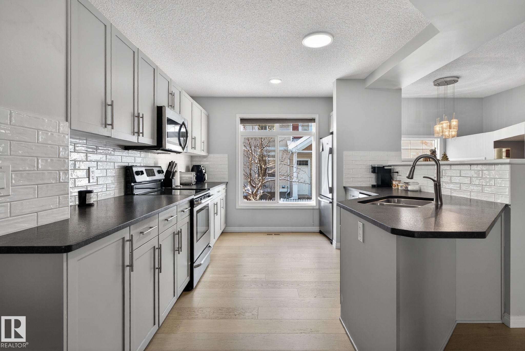 Kitchen featuring a peninsula, stainless steel appliances, backsplash, light wood-style floors, and a textured ceiling - 60 1804 70 Street, Edmonton, AB - Indoor Photo Showing Kitchen With Upgraded Kitchen