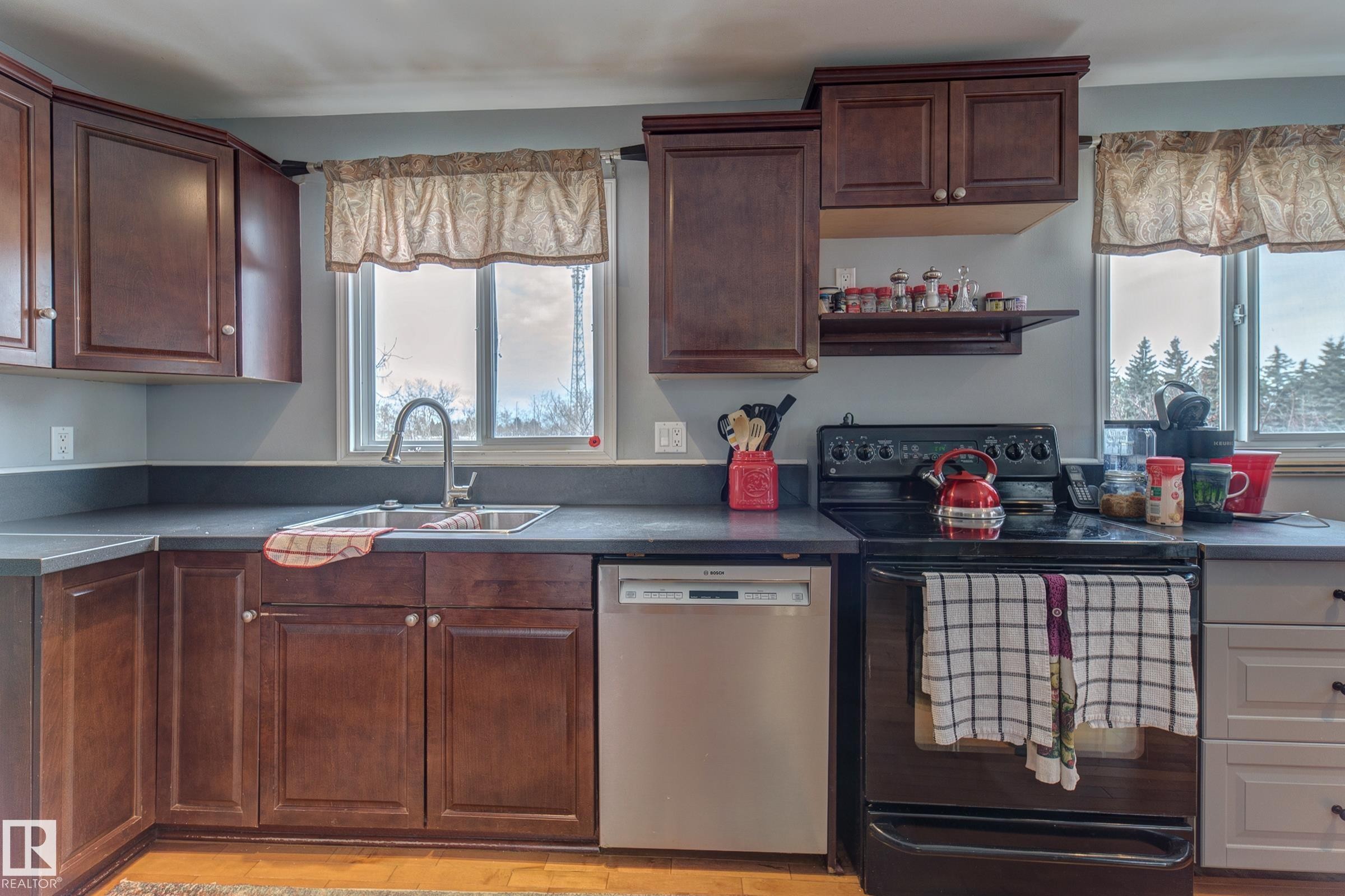 Kitchen featuring black range with electric cooktop, dishwasher, dark countertops, and light wood-style floors - 4823 10 Avenue, Edmonton, AB - Indoor Photo Showing Kitchen With Double Sink