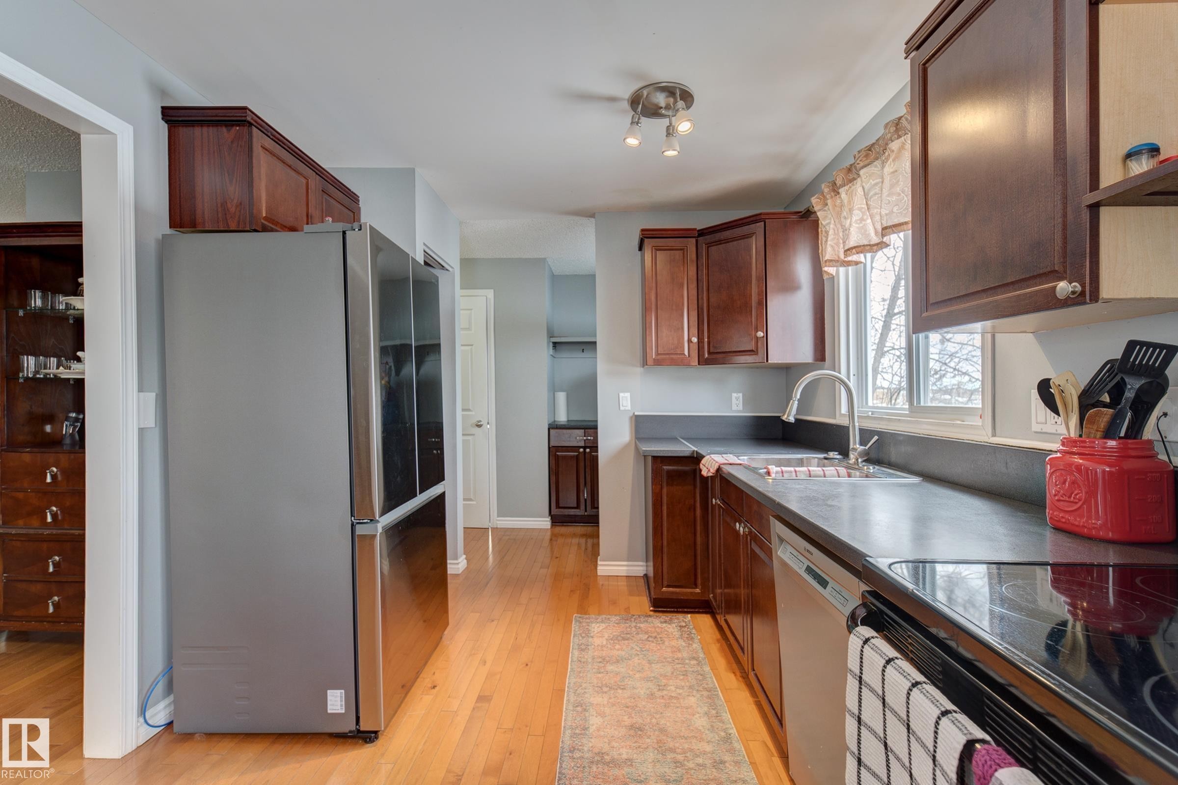 Kitchen featuring stainless steel appliances, light wood-type flooring, dark countertops, and exhaust hood - 4823 10 Avenue, Edmonton, AB - Indoor Photo Showing Kitchen