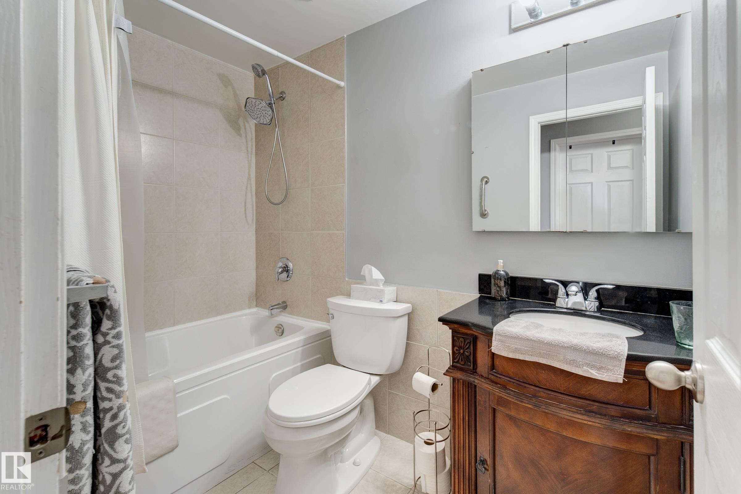 Full bathroom with vanity, shower / bath combo with shower curtain, tile walls, light tile patterned flooring, and wainscoting - 4823 10 Avenue, Edmonton, AB - Indoor Photo Showing Bathroom