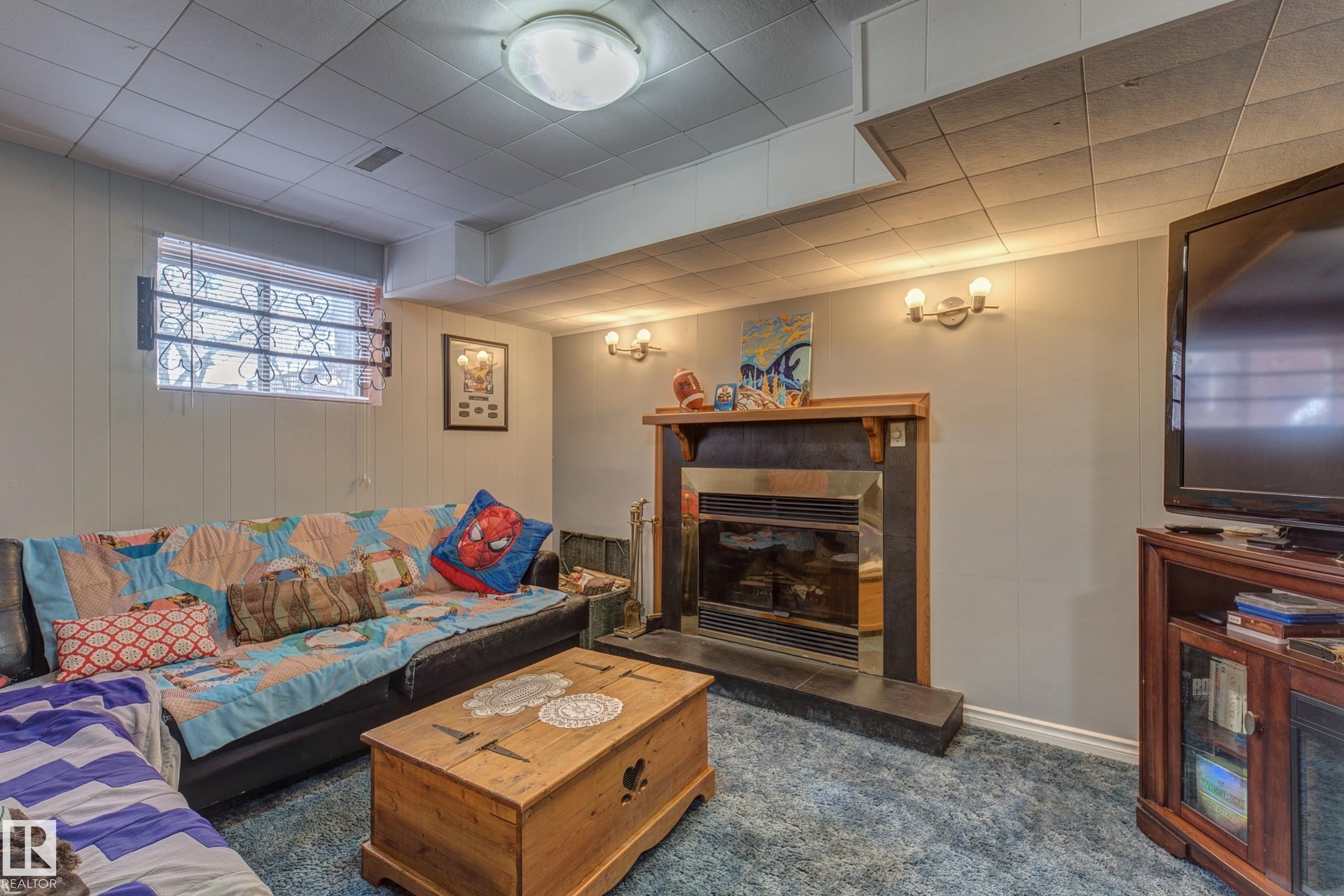 Living room with a fireplace, dark carpet, and wood walls - 4823 10 Avenue, Edmonton, AB - Indoor Photo Showing Living Room With Fireplace