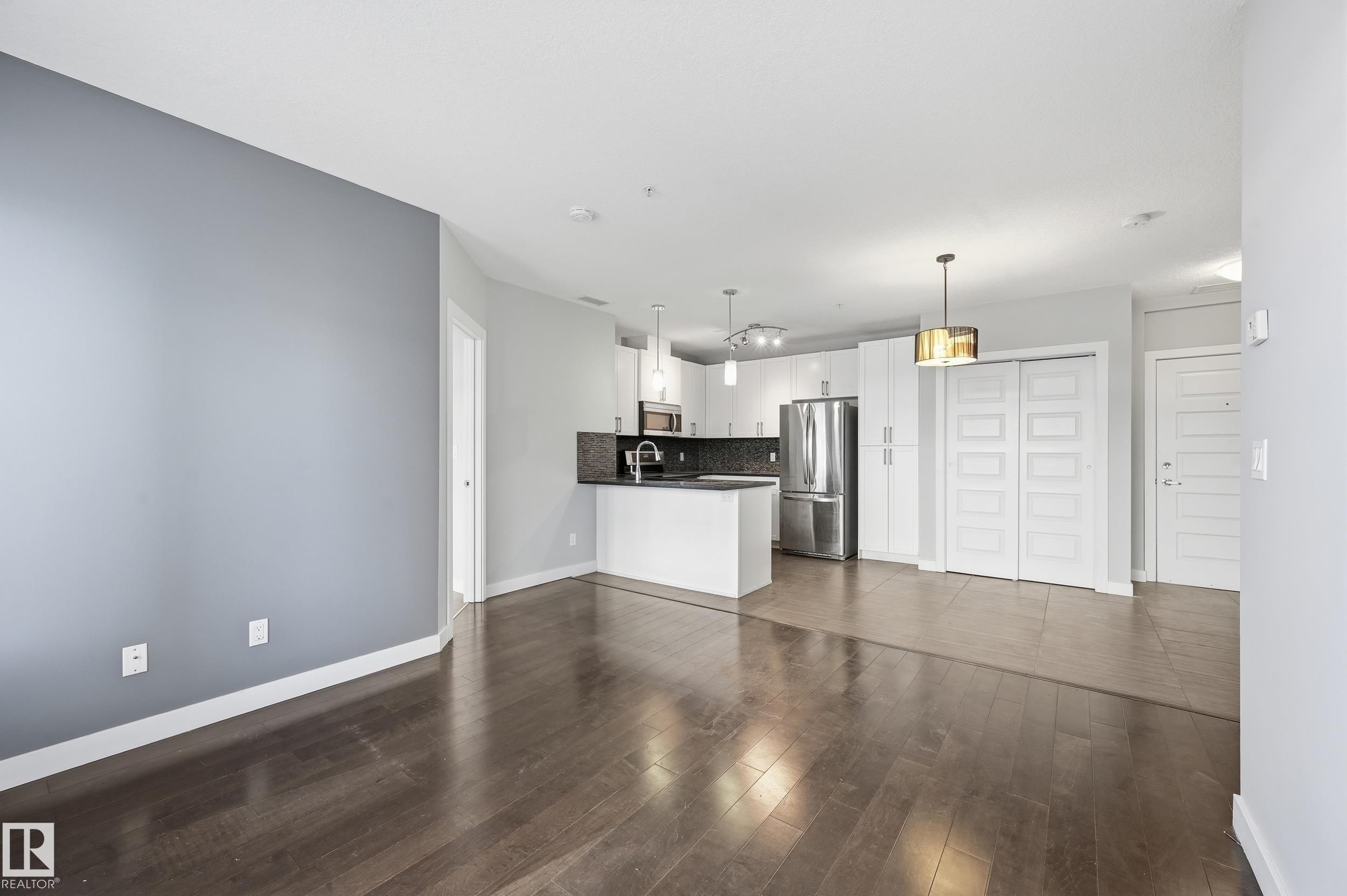 Unfurnished living room with dark wood finished floors and baseboards - 511 5151 Windermere Boulevard, Edmonton, AB - Indoor Photo Showing Kitchen