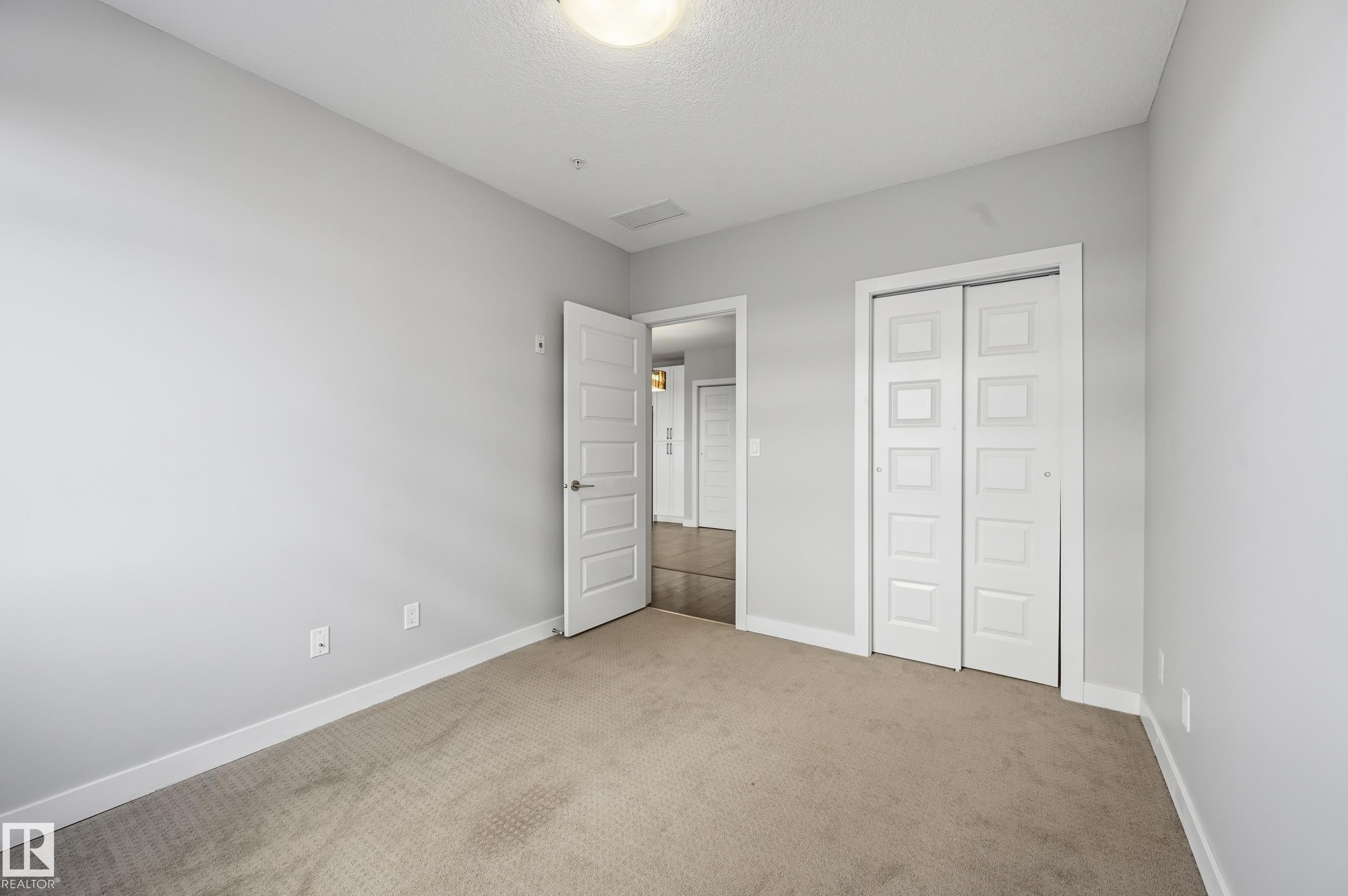 Unfurnished bedroom with light colored carpet, a closet, and a textured ceiling - 511 5151 Windermere Boulevard, Edmonton, AB - Indoor Photo Showing Other Room