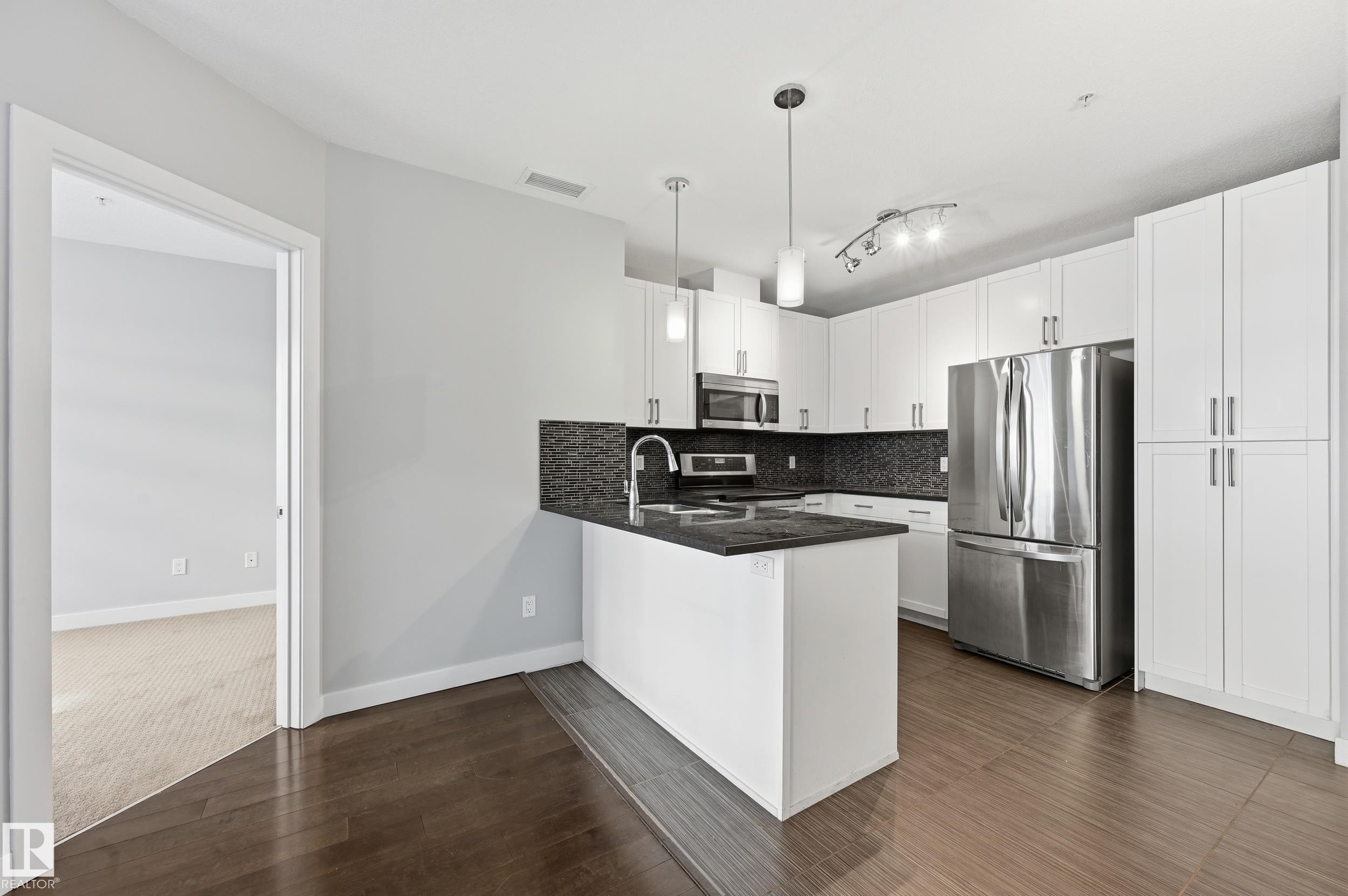 Kitchen featuring white cabinetry, stainless steel appliances, dark stone counters, and decorative backsplash - 511 5151 Windermere Boulevard, Edmonton, AB - Indoor Photo Showing Kitchen