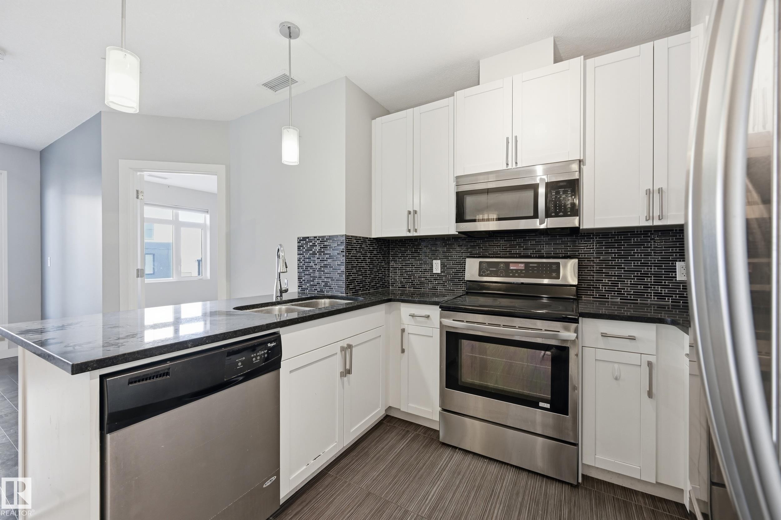 Kitchen featuring stainless steel appliances, a peninsula, white cabinets, and dark stone countertops - 511 5151 Windermere Boulevard, Edmonton, AB - Indoor Photo Showing Kitchen With Double Sink With Upgraded Kitchen