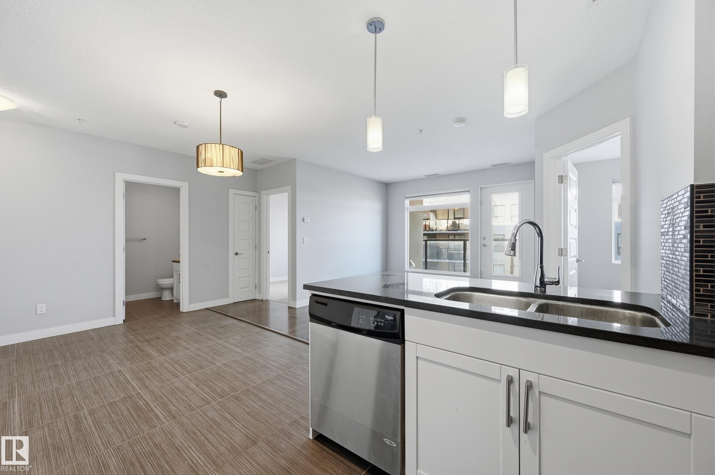 Kitchen with dishwasher, pendant lighting, white cabinets, and dark stone countertops - 511 5151 Windermere Boulevard, Edmonton, AB - Indoor Photo Showing Kitchen With Double Sink