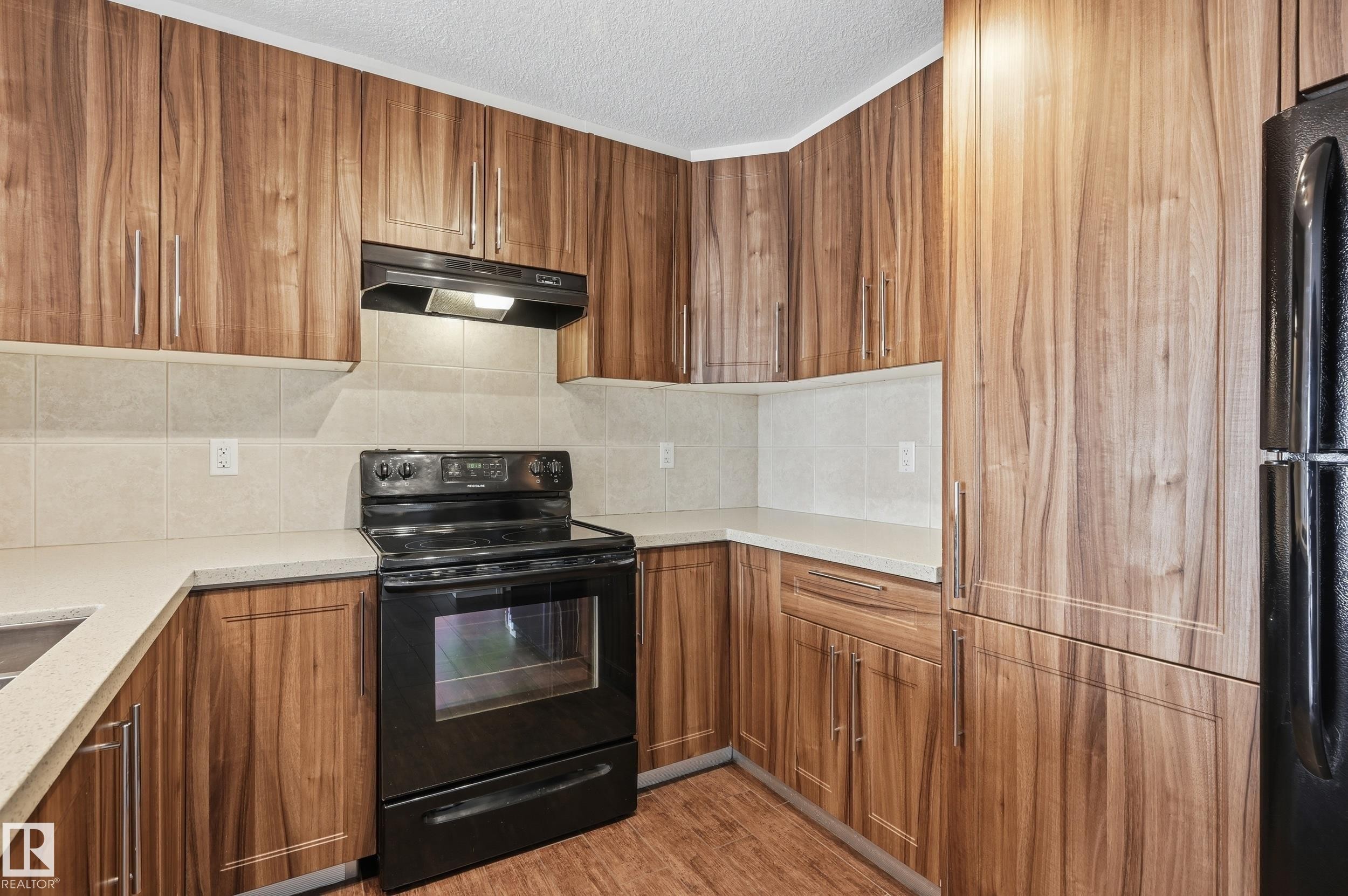 Kitchen with black appliances, wood finish cabinetry, a textured ceiling, backsplash, and light stone counters - 1351 Cunningham Drive, Edmonton, AB - Indoor Photo Showing Kitchen