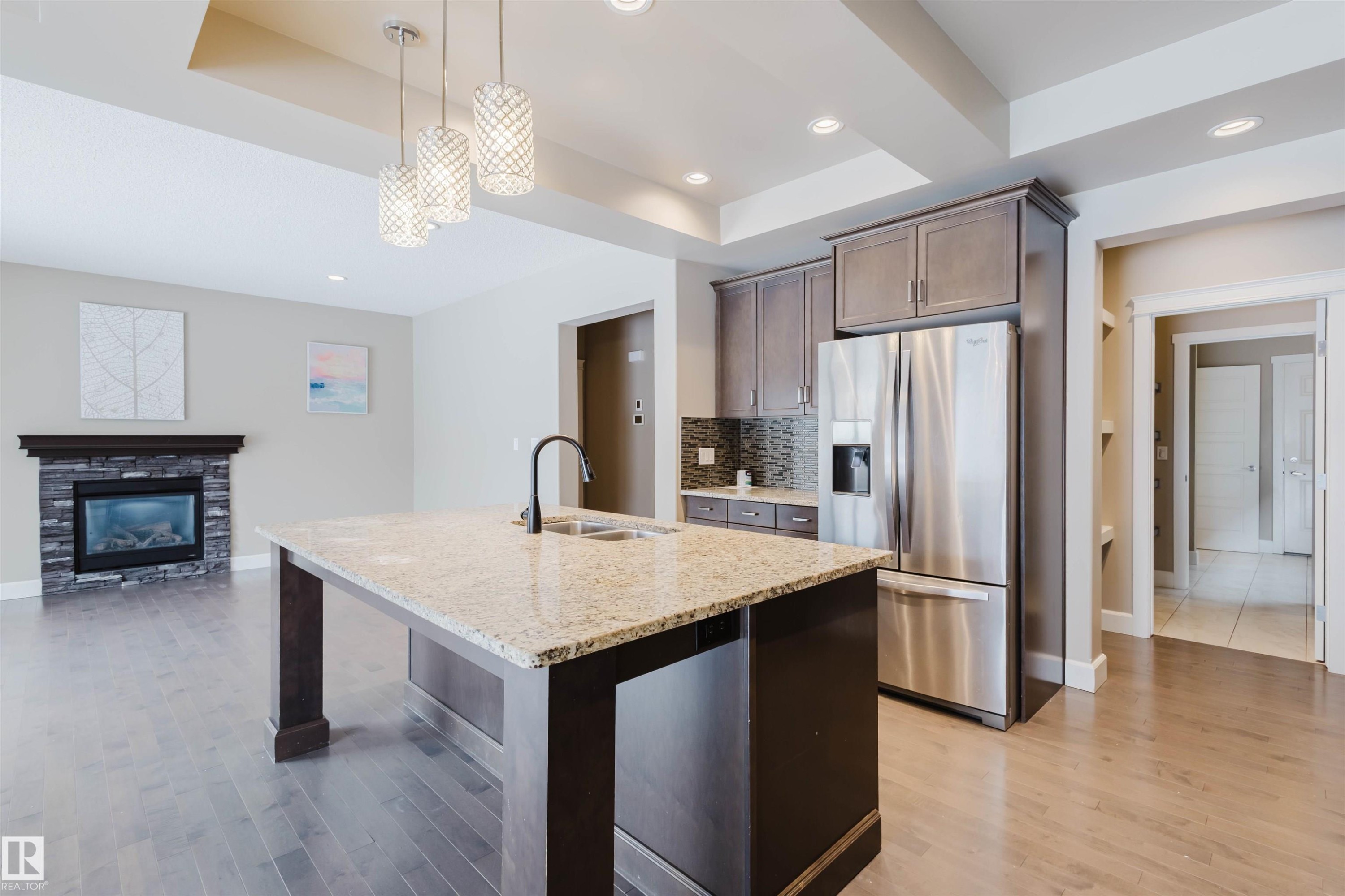 Kitchen with stainless steel fridge with ice dispenser, open floor plan, light stone counters, a raised ceiling, and a kitchen island with sink - 1957 Ainslie Link, Edmonton, AB - Indoor Photo Showing Kitchen With Stainless Steel Kitchen With Double Sink With Upgraded Kitchen