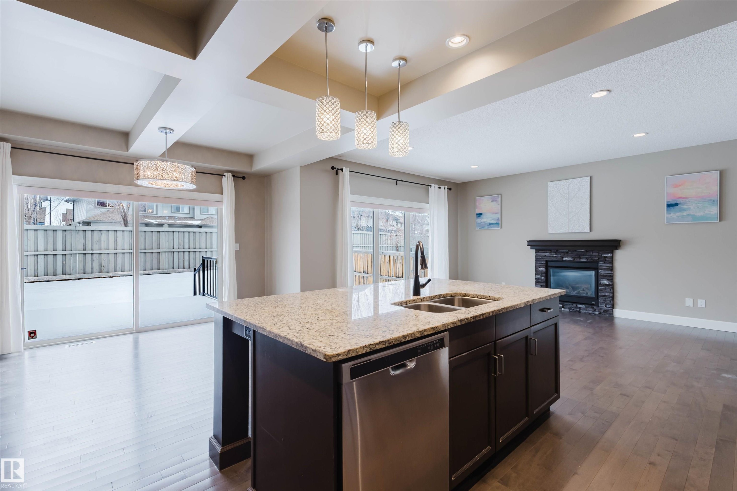 Kitchen with open floor plan, stainless steel dishwasher, dark wood finished floors, pendant lighting, and light stone counters - 1957 Ainslie Link, Edmonton, AB - Indoor Photo Showing Kitchen With Fireplace With Double Sink