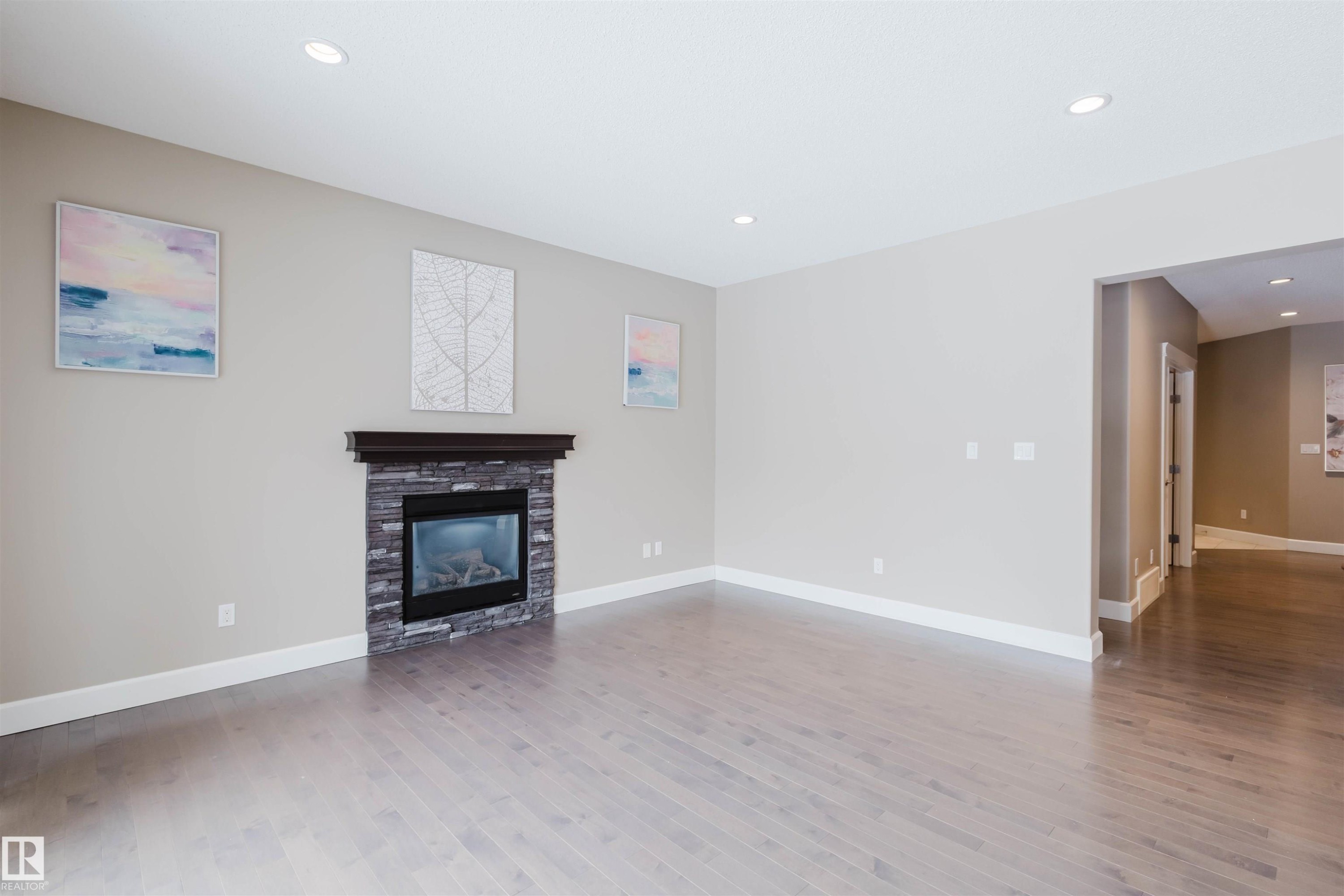 Unfurnished living room featuring recessed lighting, light wood-style flooring, and a stone fireplace - 1957 Ainslie Link, Edmonton, AB - Indoor Photo Showing Living Room With Fireplace