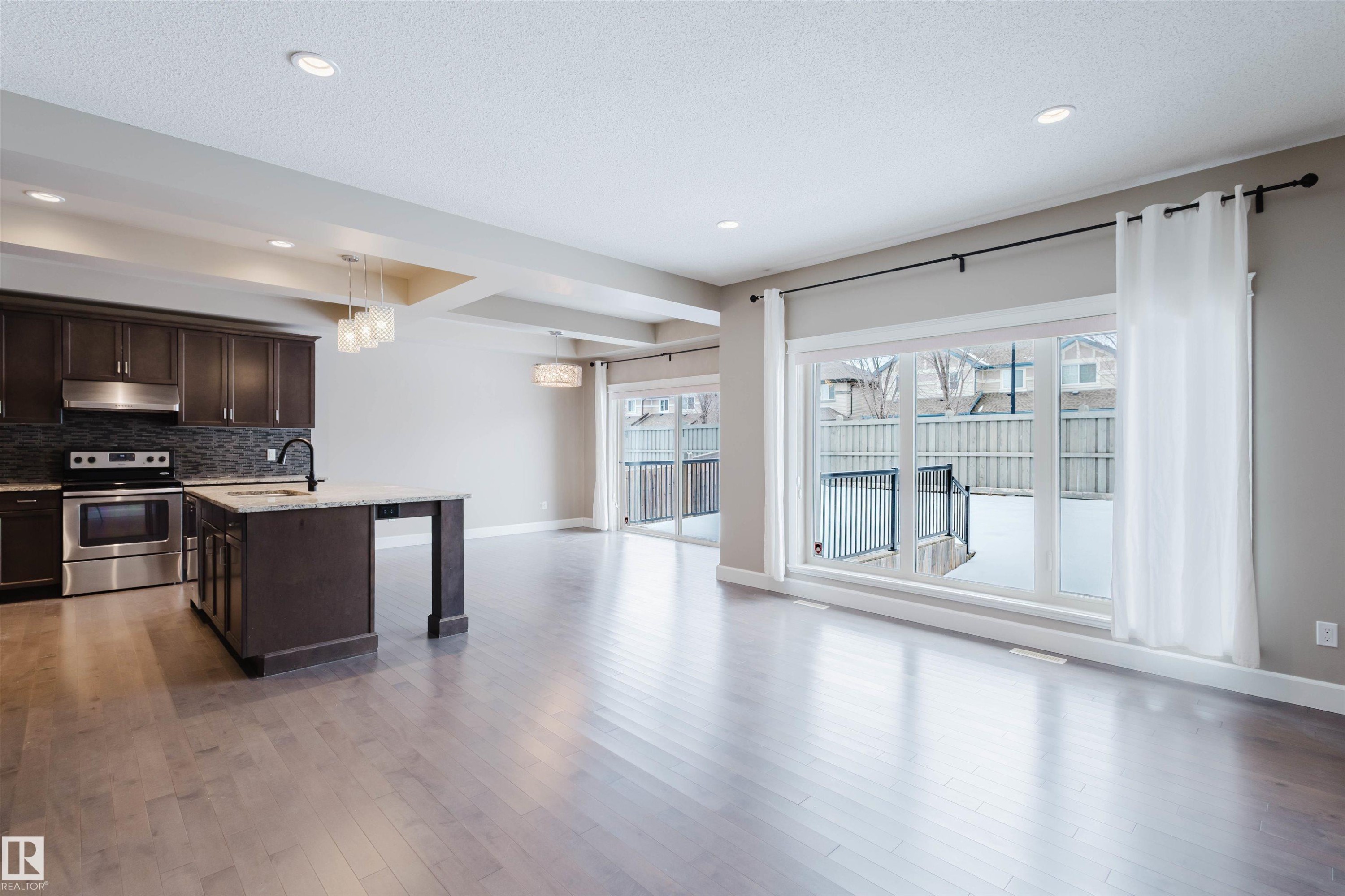 Kitchen with healthy amount of natural light, dark wood finish cabinetry, stainless steel electric range oven, and an island with sink - 1957 Ainslie Link, Edmonton, AB - Indoor Photo Showing Kitchen