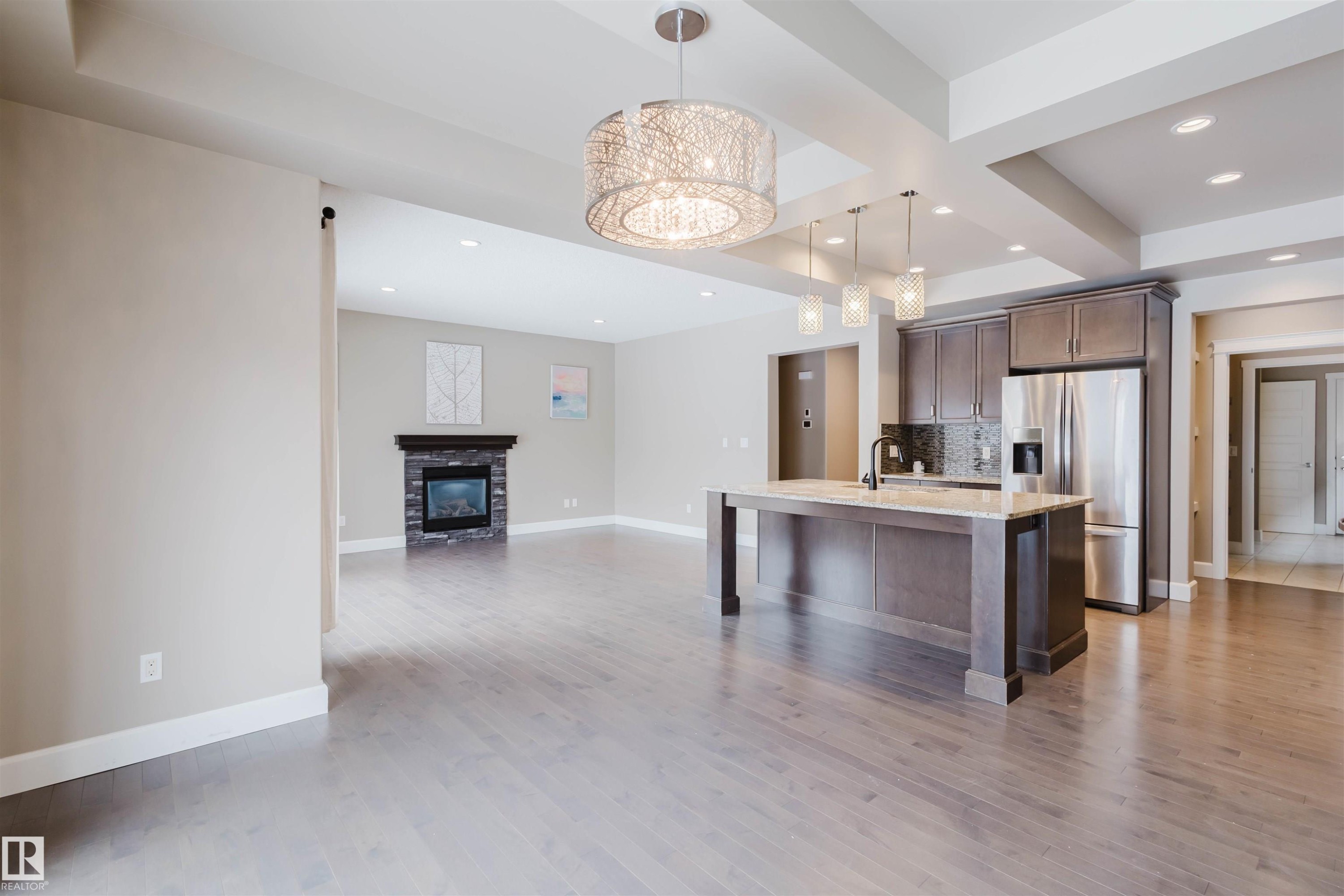 Kitchen with open floor plan, an island with sink, stainless steel fridge with ice dispenser, light stone counters, and a breakfast bar - 1957 Ainslie Link, Edmonton, AB - Indoor Photo Showing Kitchen