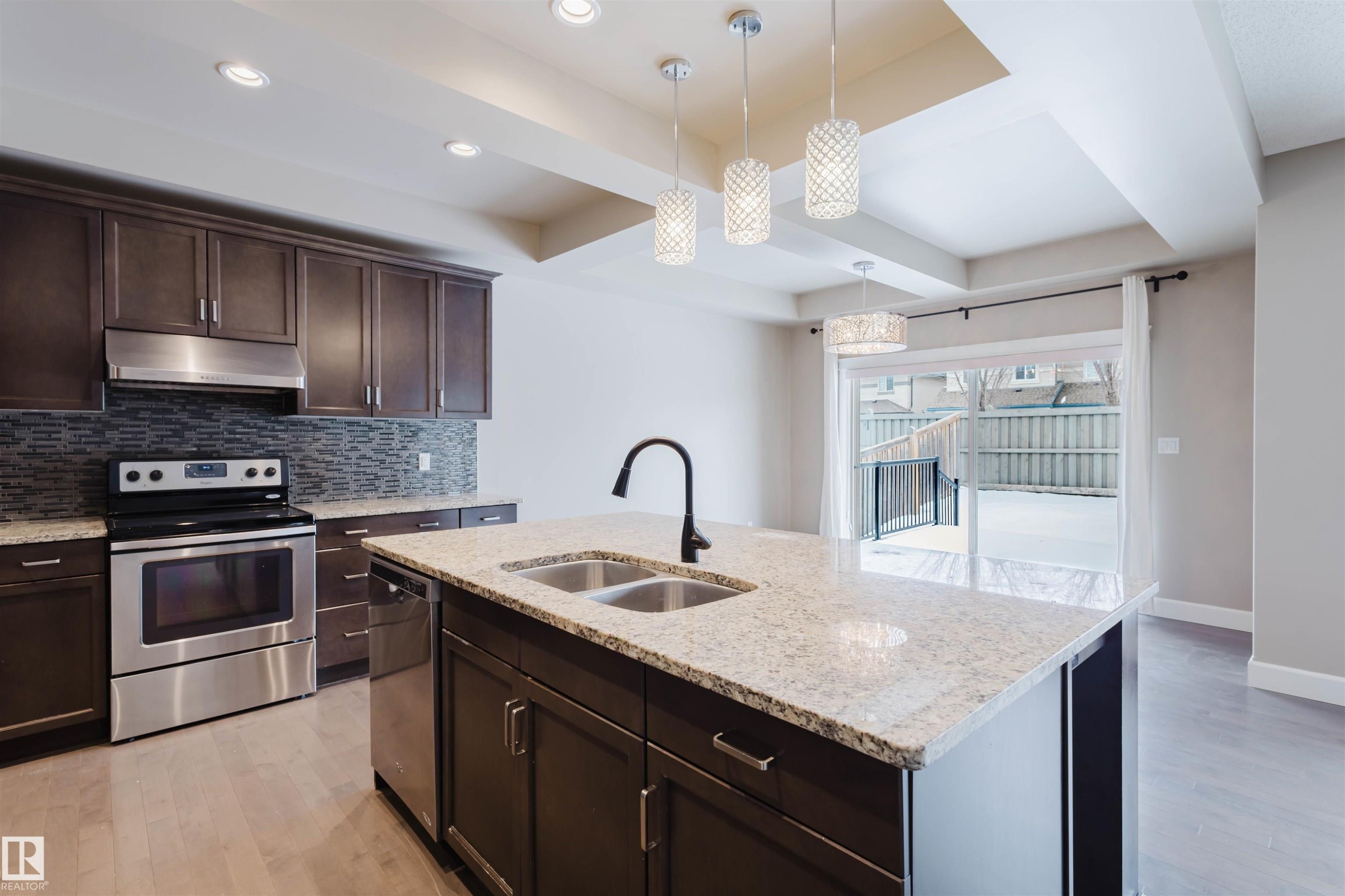 Kitchen featuring dark wood finish cabinets, stainless steel appliances, light wood-style flooring, light stone countertops, and coffered ceiling - 1957 Ainslie Link, Edmonton, AB - Indoor Photo Showing Kitchen With Double Sink With Upgraded Kitchen