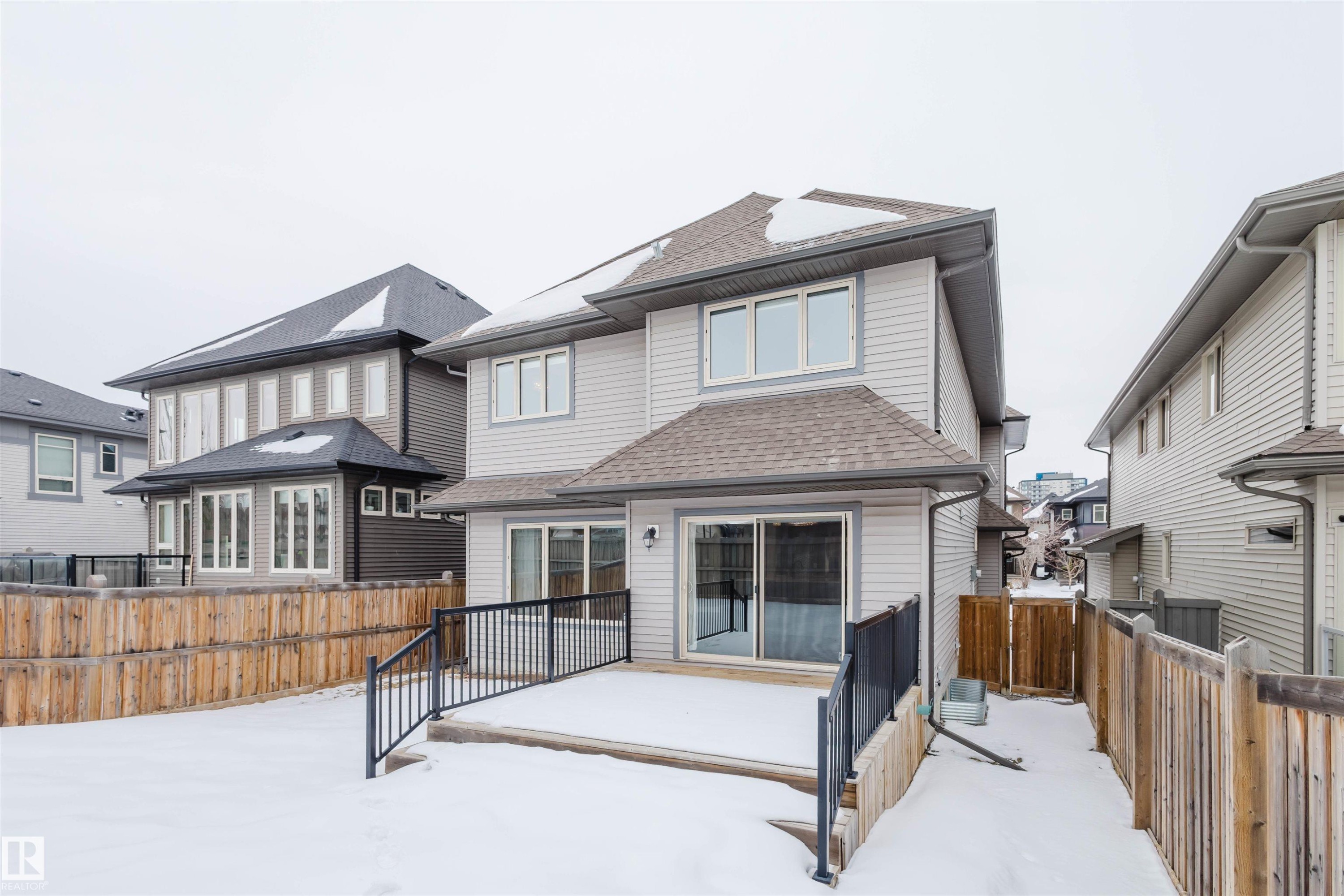 Snow covered house with a shingled roof, a wooden deck, and a fenced backyard - 1957 Ainslie Link, Edmonton, AB - Outdoor With Exterior