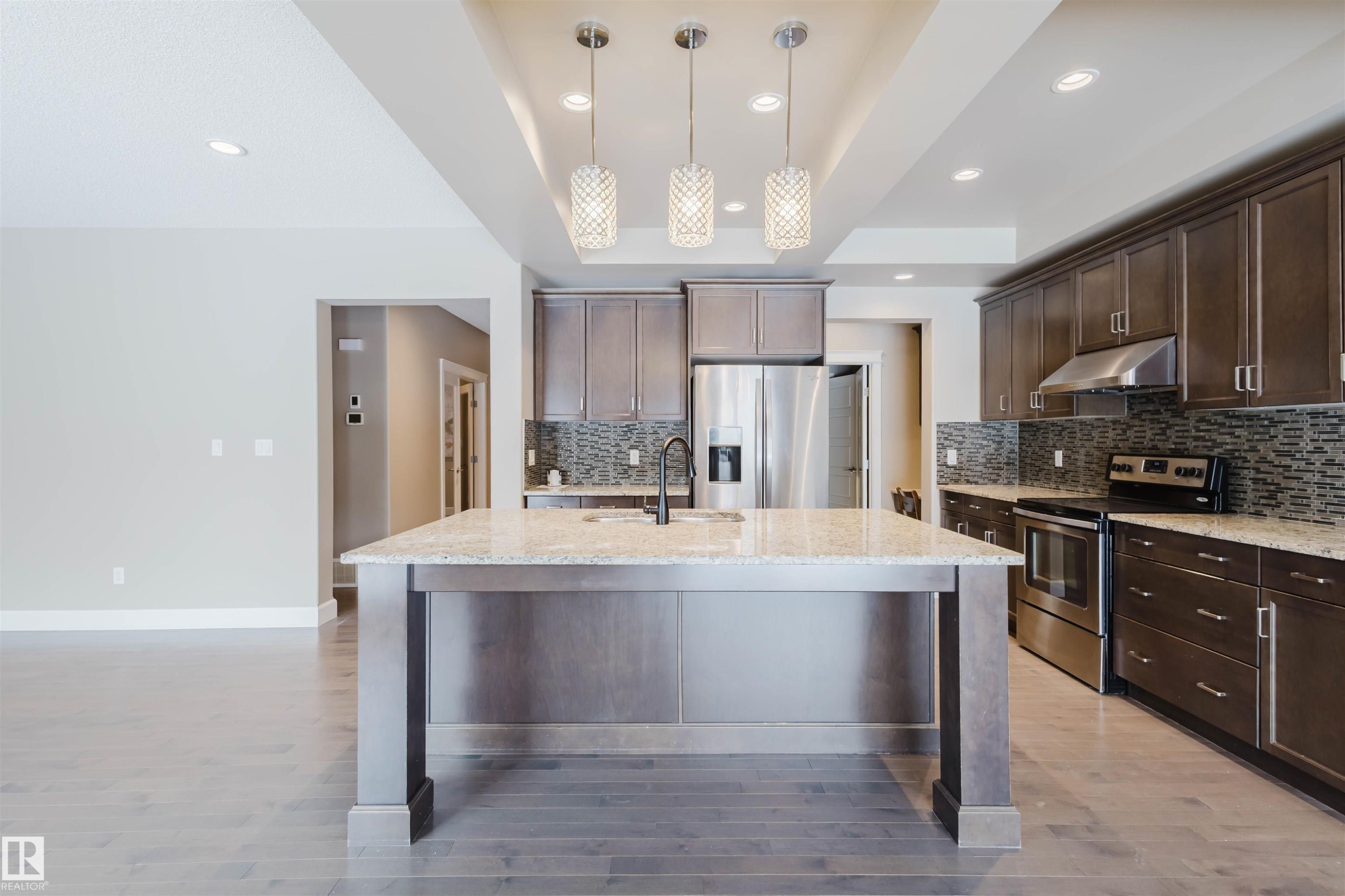 Kitchen with stainless steel appliances, dark wood finish cabinetry, light stone counters, light wood finished floors, and a raised ceiling - 1957 Ainslie Link, Edmonton, AB - Indoor Photo Showing Kitchen With Stainless Steel Kitchen With Upgraded Kitchen
