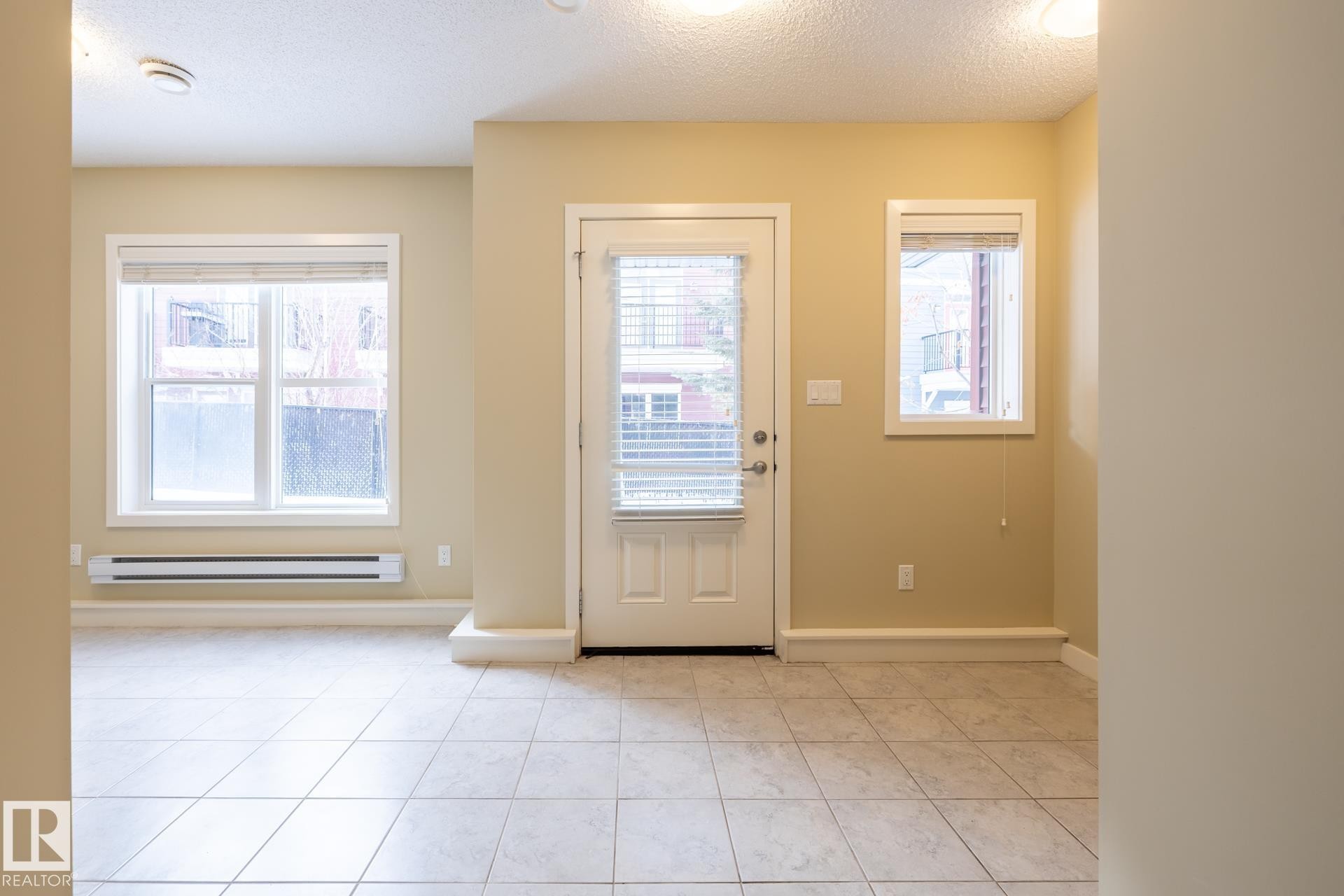 Entrance foyer featuring a textured ceiling, a baseboard heating unit, and light tile patterned flooring - 21 655 Watt Boulevard, Edmonton, AB - Indoor Photo Showing Other Room