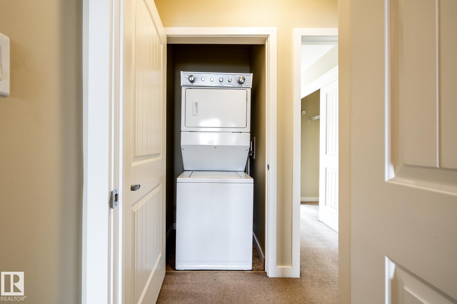 Laundry area featuring light carpet and stacked washer and clothes dryer - 21 655 Watt Boulevard, Edmonton, AB - Indoor Photo Showing Laundry Room